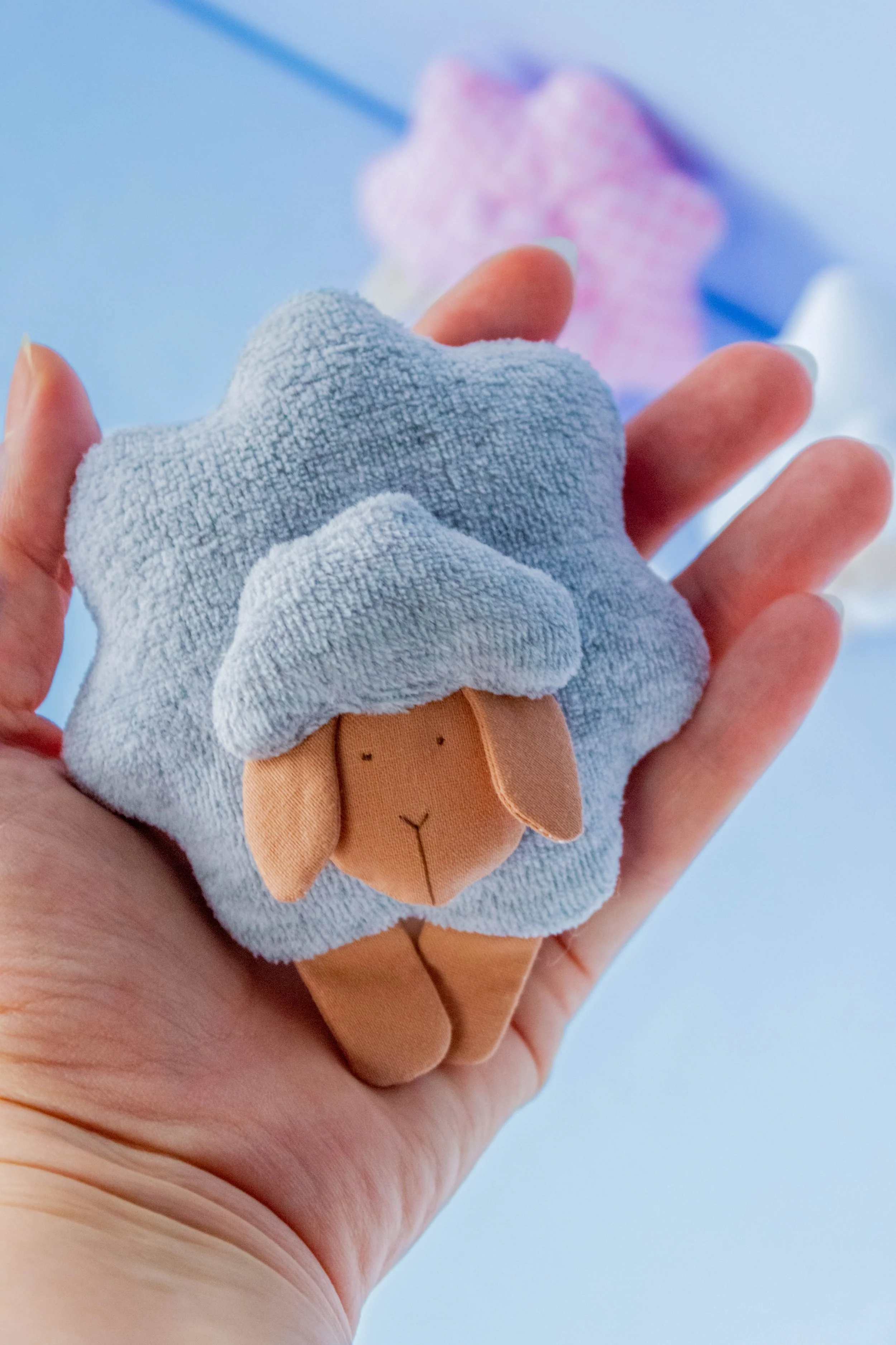 A person's hand holding a small plush toy of a lion with a grey blanket wrapped around it, against a blue background.