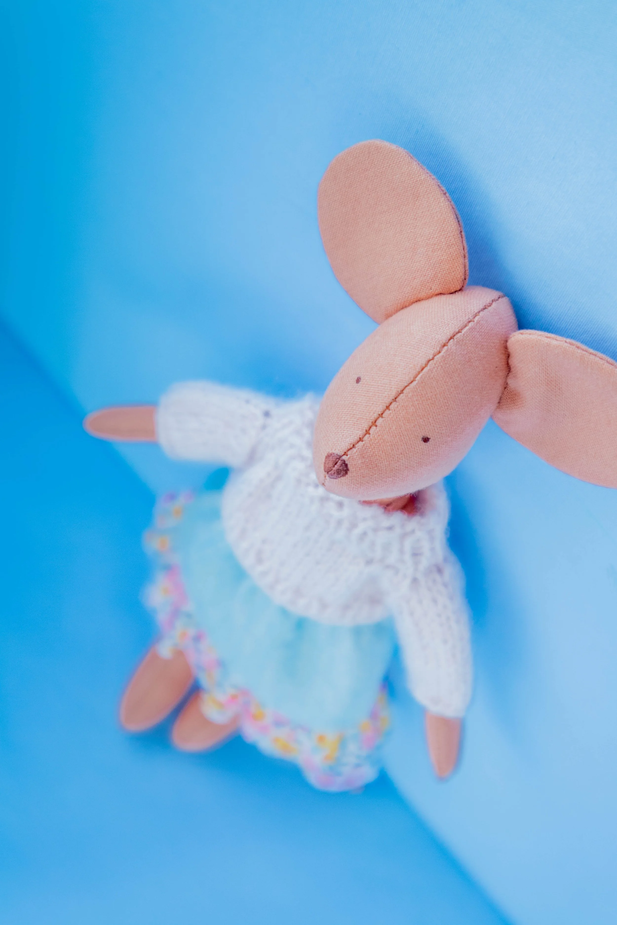 Close-up of a plush unicorn toy with a peach-colored body, white horn with rainbow accents, and white knitted tail against a bright blue background.
