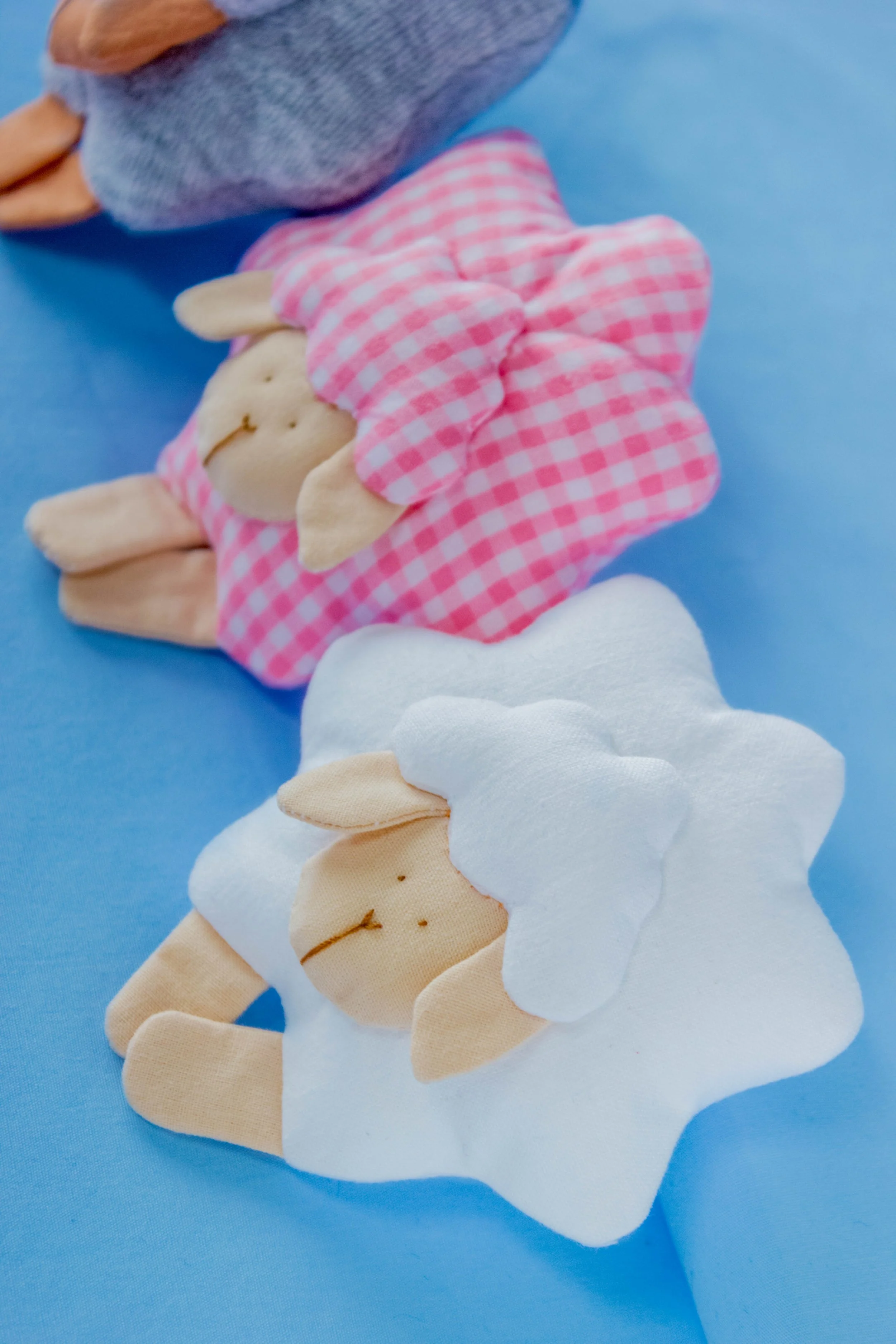 Close-up of three colorful plush unicorn toys on a blue background with white clouds and a sun, made from soft fabric with stitched details.