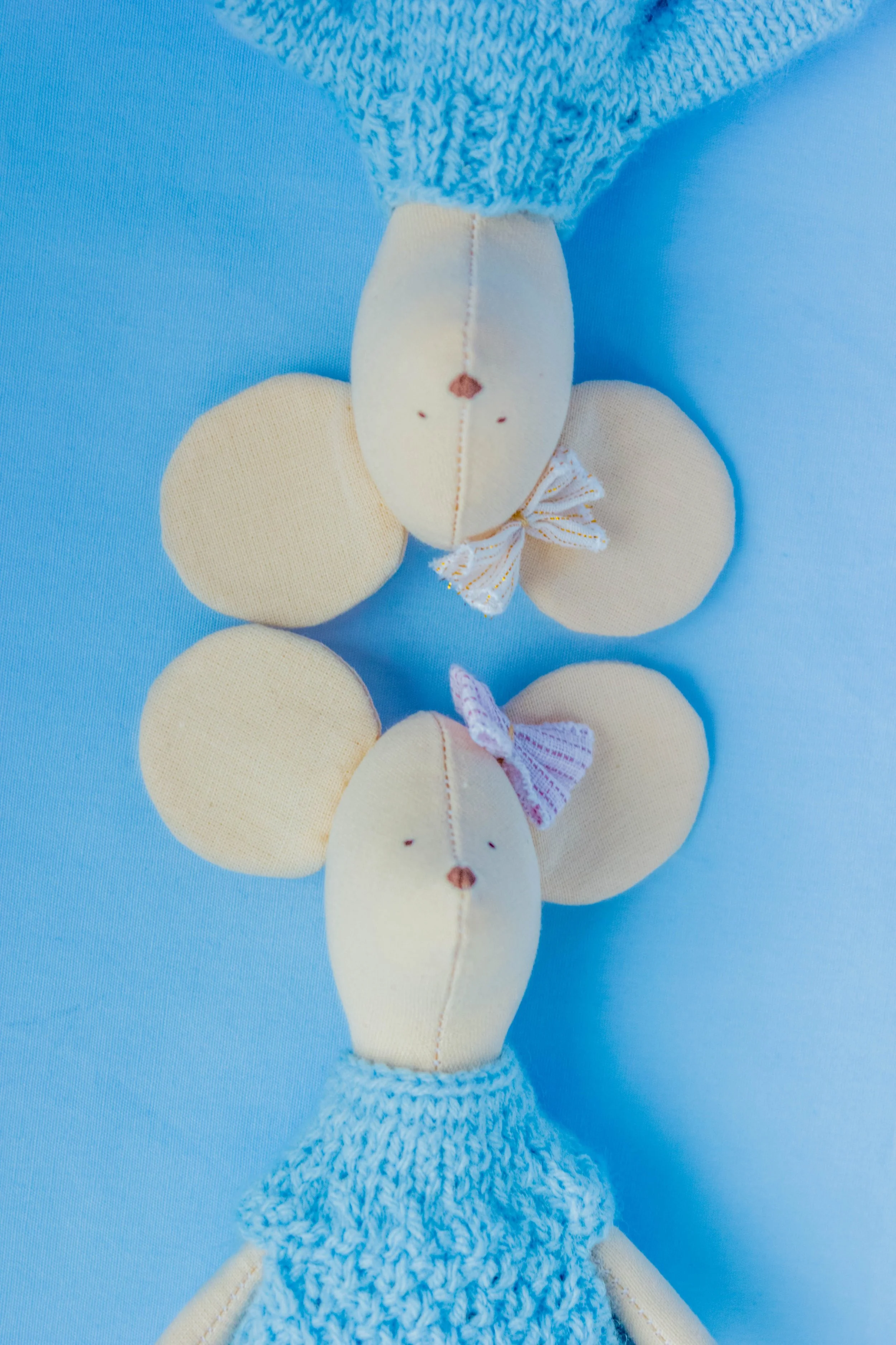 Close-up of a fabric toy giraffe with blue and cream colors, featuring small bows, set against a light blue background.