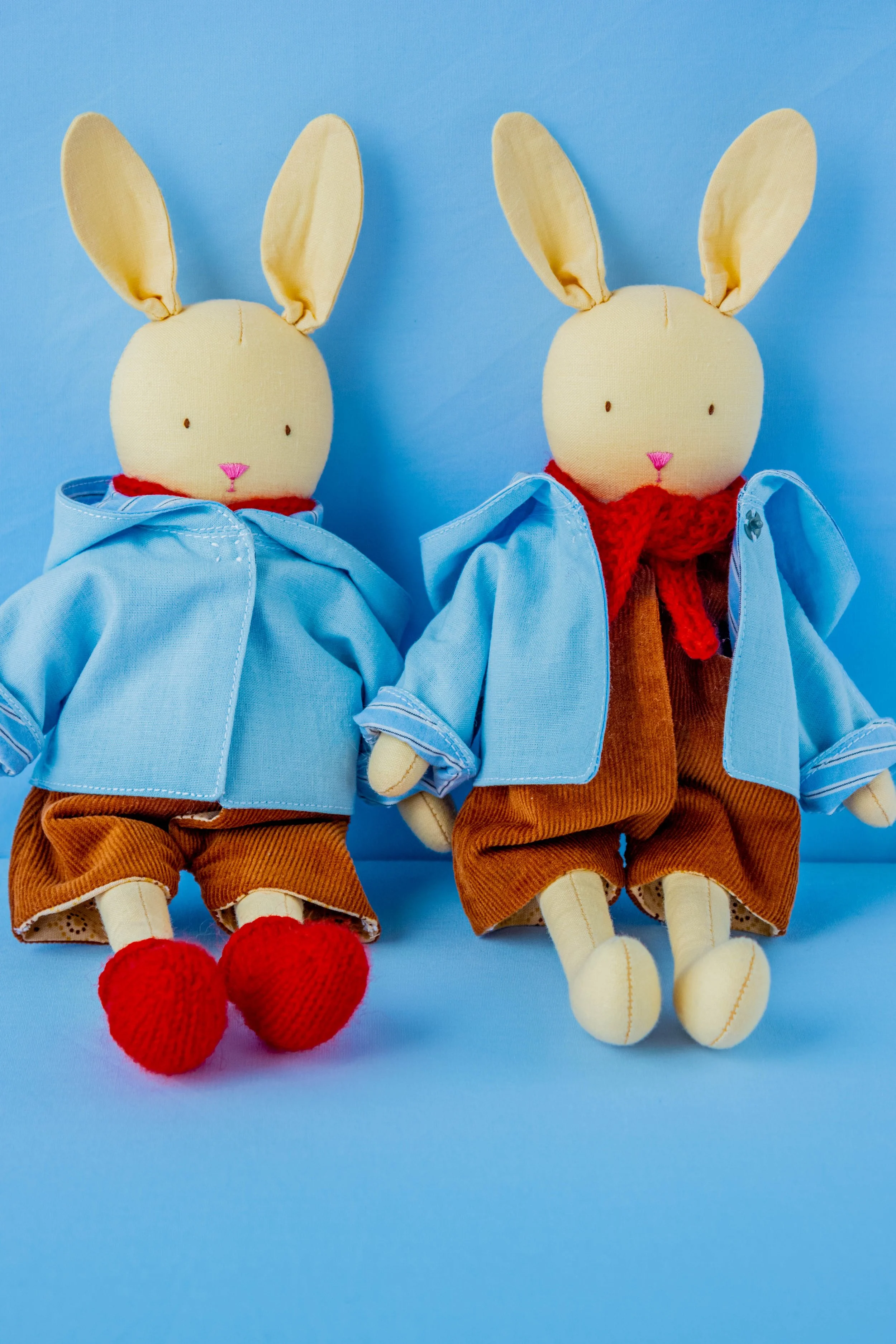 Two stuffed bunny dolls dressed in blue and brown clothing, sitting against a blue background.