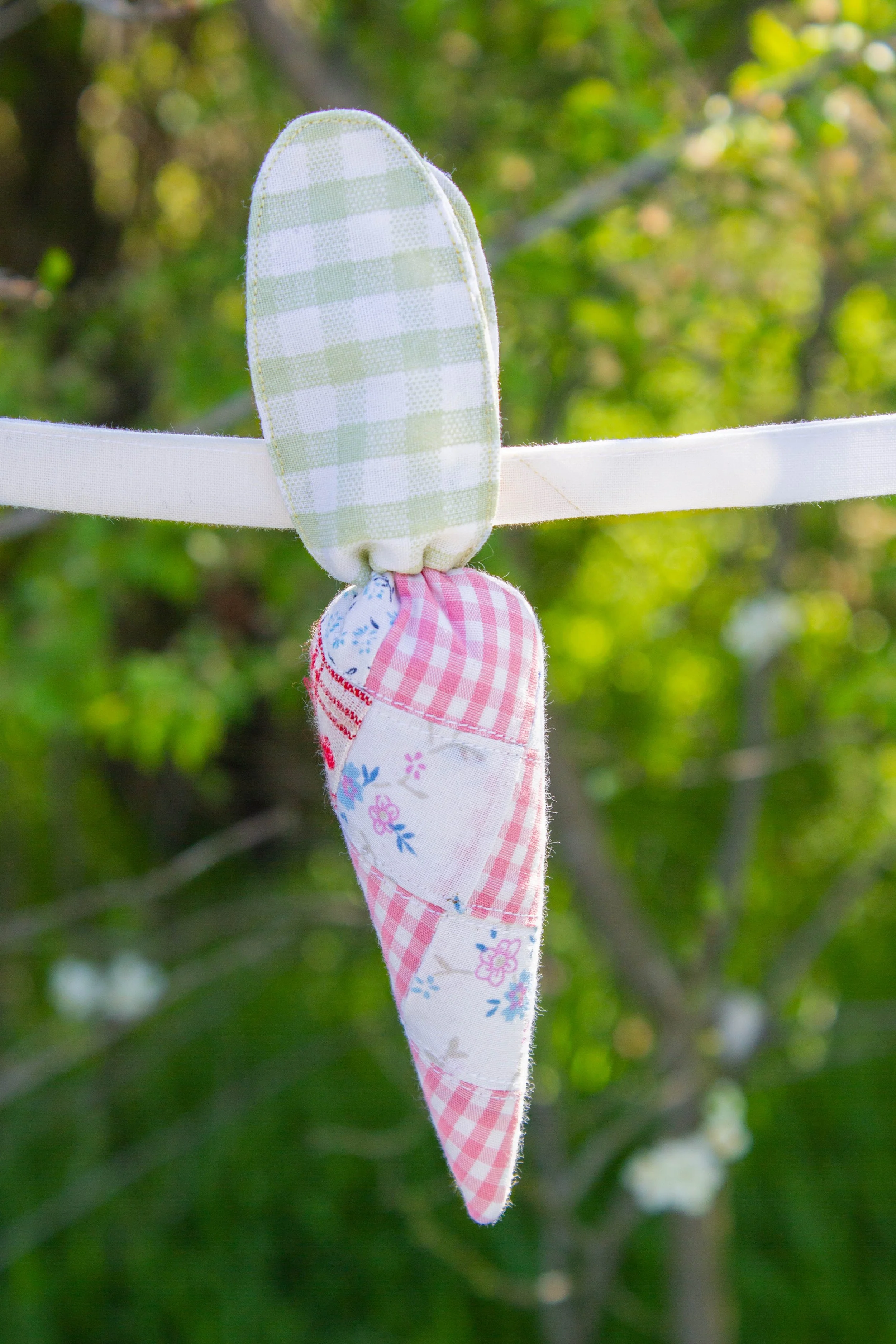 Colorful fabric iPod-shaped ribbons hanging on a white string against a blurred green leafy background.