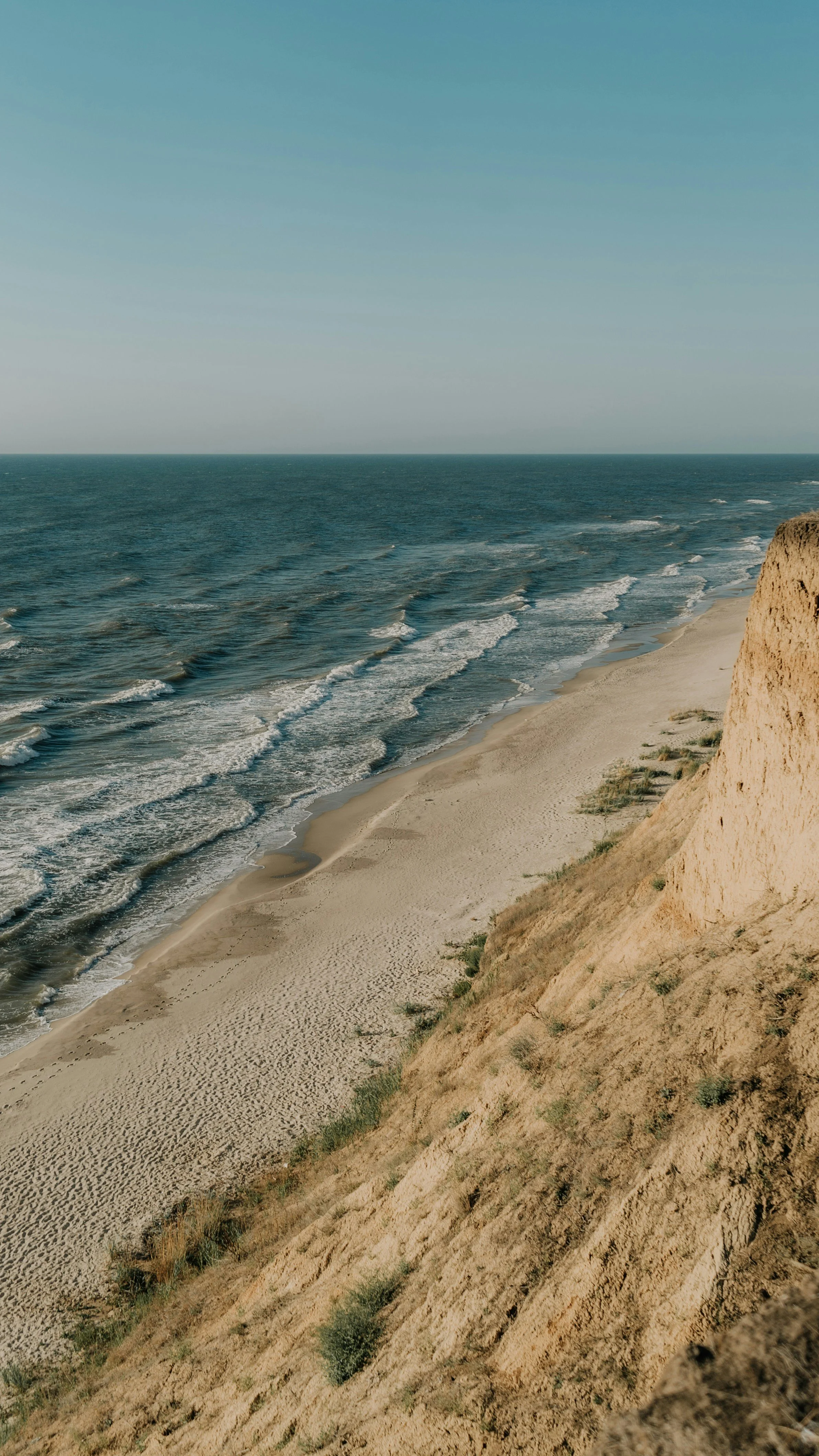 Ocean shoreline with waves hitting the sandy beach and a sandy cliff on the right side of the image.