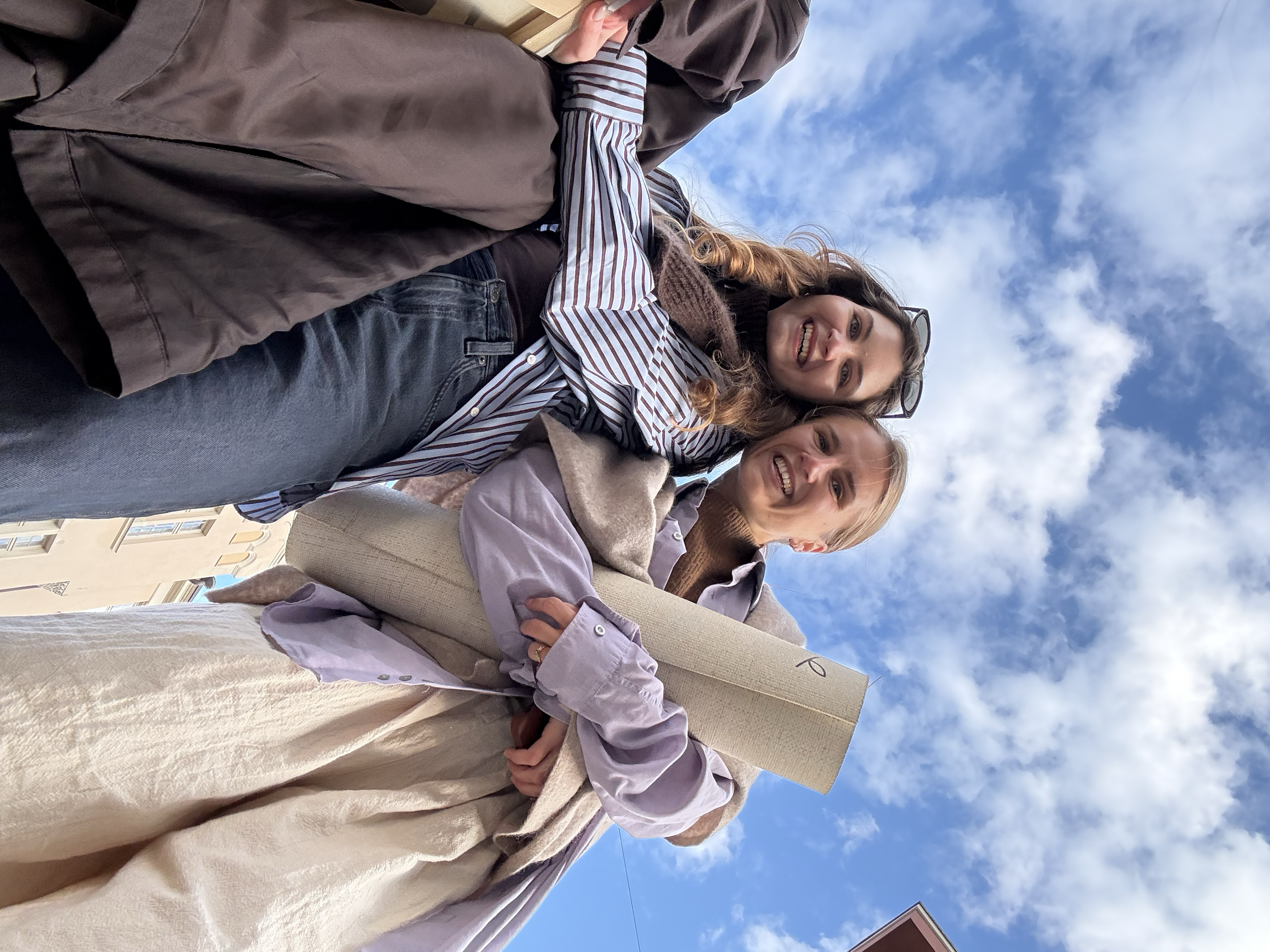 Two women smiling and outdoors, with a blue sky and some clouds behind them.