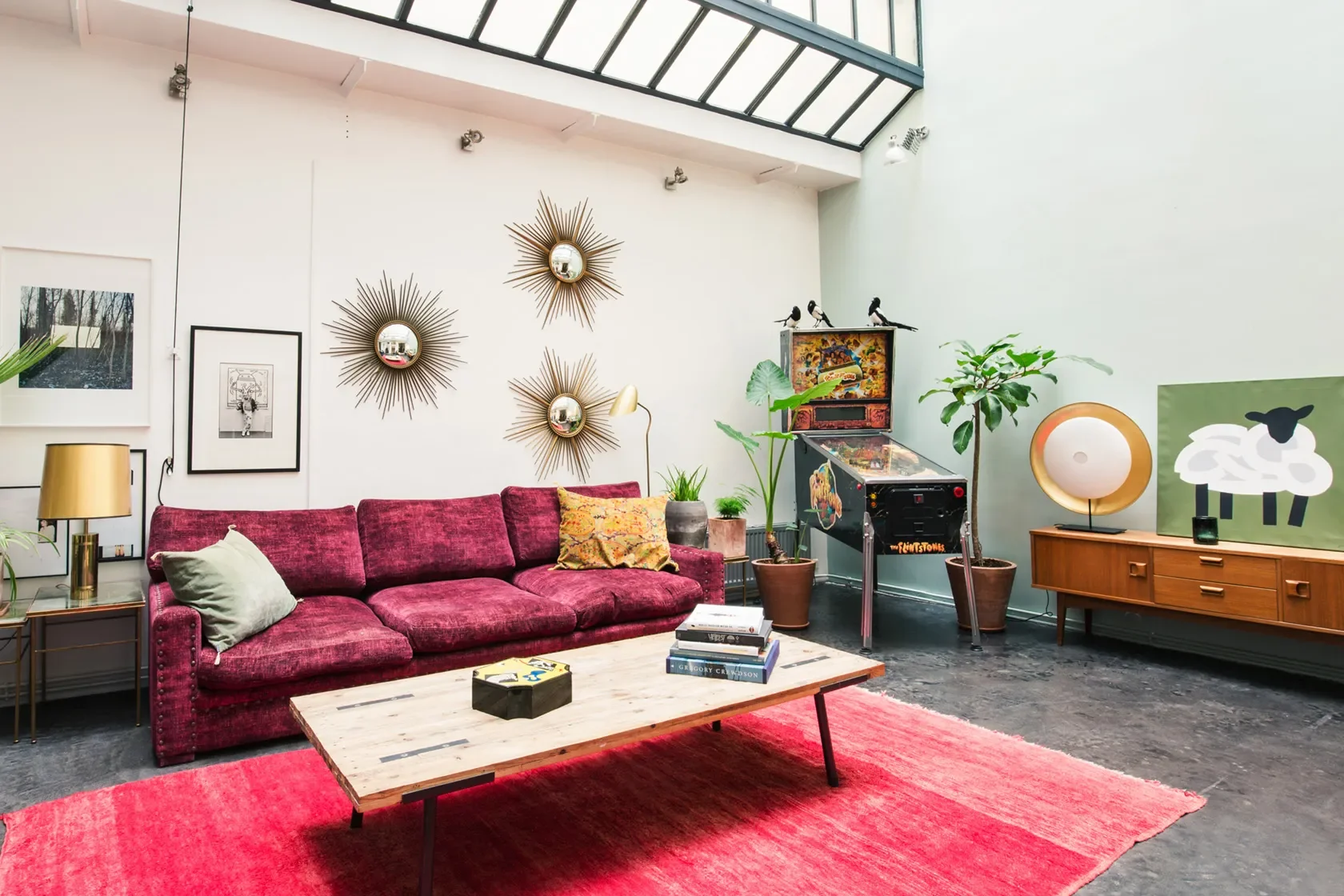 Séjour sous verrière d'artiste avec canapé fuchsia, flipper vintage et miroirs soleil, loft Batignolles par DMM Interiors.