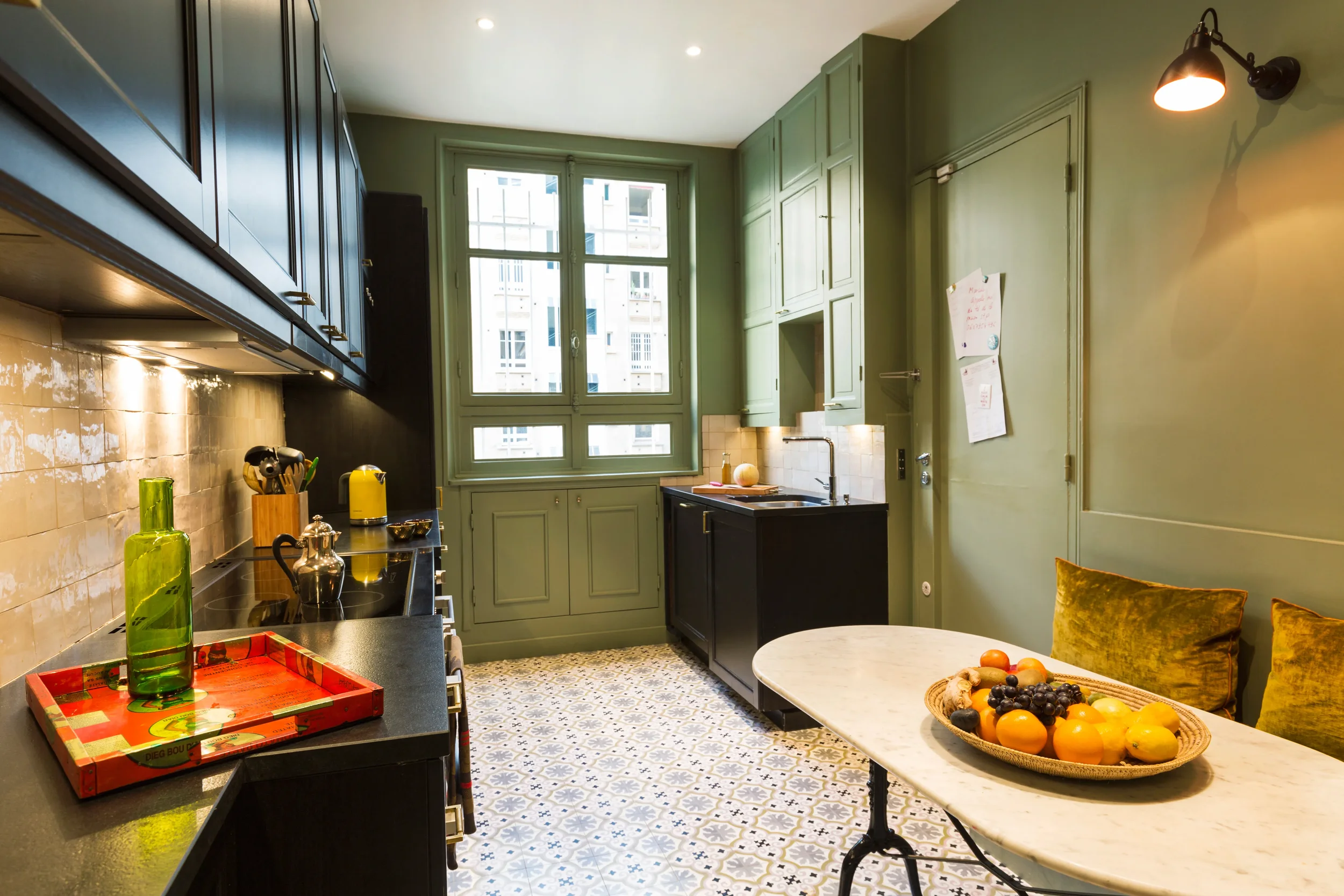 Cuisine dinatoire sur-mesure aux teintes vert sauge et noir, sol en carreaux de ciment, projet Neuilly par DMM Interiors.