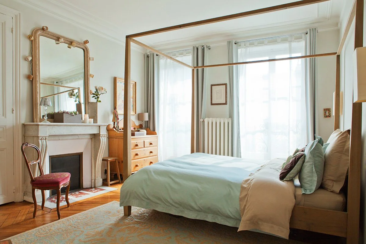 Chambre haussmannienne avec lit à baldaquin en bois, cheminée en marbre et parquet Point de Hongrie au Canal Saint-Martin.