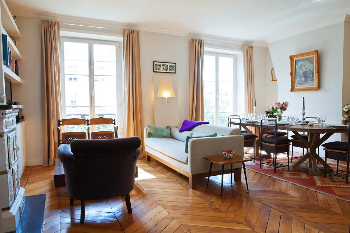 Espace de vie chaleureux avec parquet en point de Hongrie, poêle ancien en faïence, canapé contemporain et grande table à manger en bois dans un appartement aux Batignolles