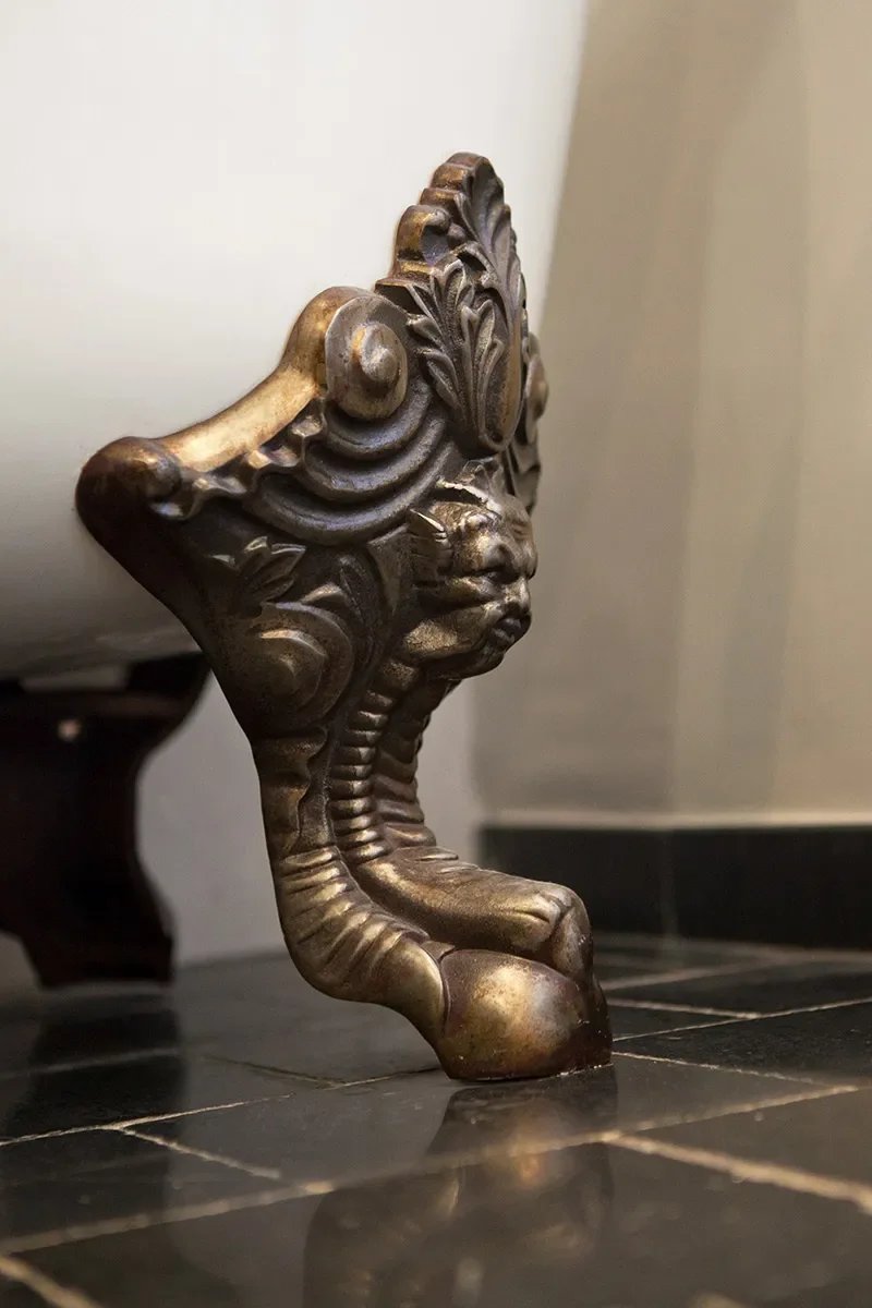 Gros plan sur un pied de baignoire îlot en fonte et laiton patiné sculpté reposant sur un sol en pierre noire