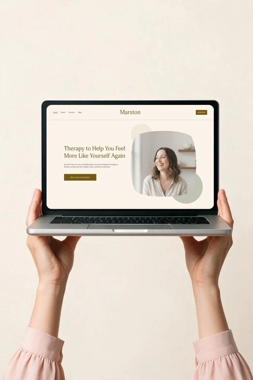 A person holding a laptop with a therapy website showing a smiling woman and the text "Therapy to Help You Feel More Like Yourself Again."