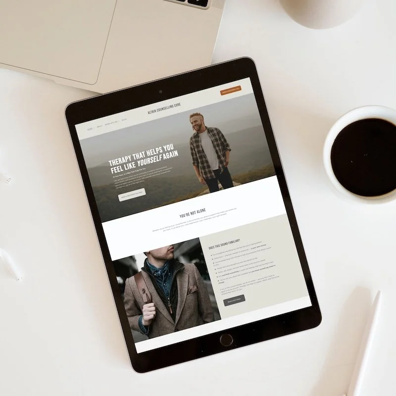 Tablet displaying Altair website template for therapists and counsellors, with a man smiling outdoors on the main banner, and a person in a blazer below. Surrounding items include a laptop, a cup of coffee, and white pens on a white desk.