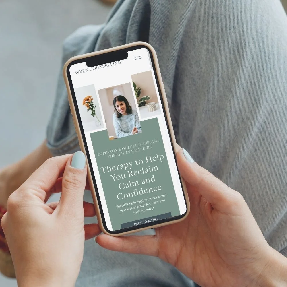 A person holding a smartphone displaying a therapy service website with images of a woman and plants, and text about in-person and online therapy services.