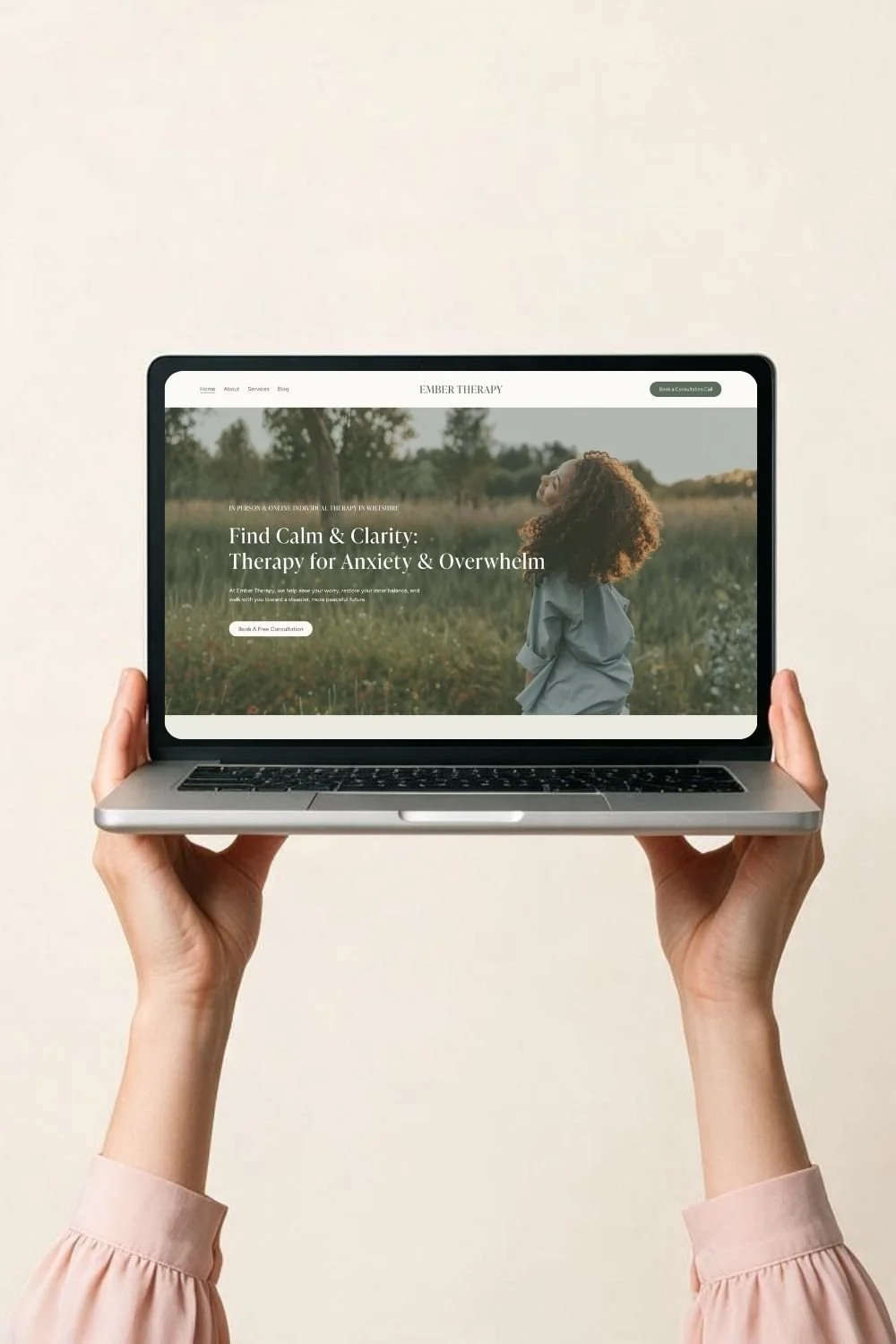 Person holding a laptop displaying a therapy website called Ember Therapy, with a woman standing in a field.
