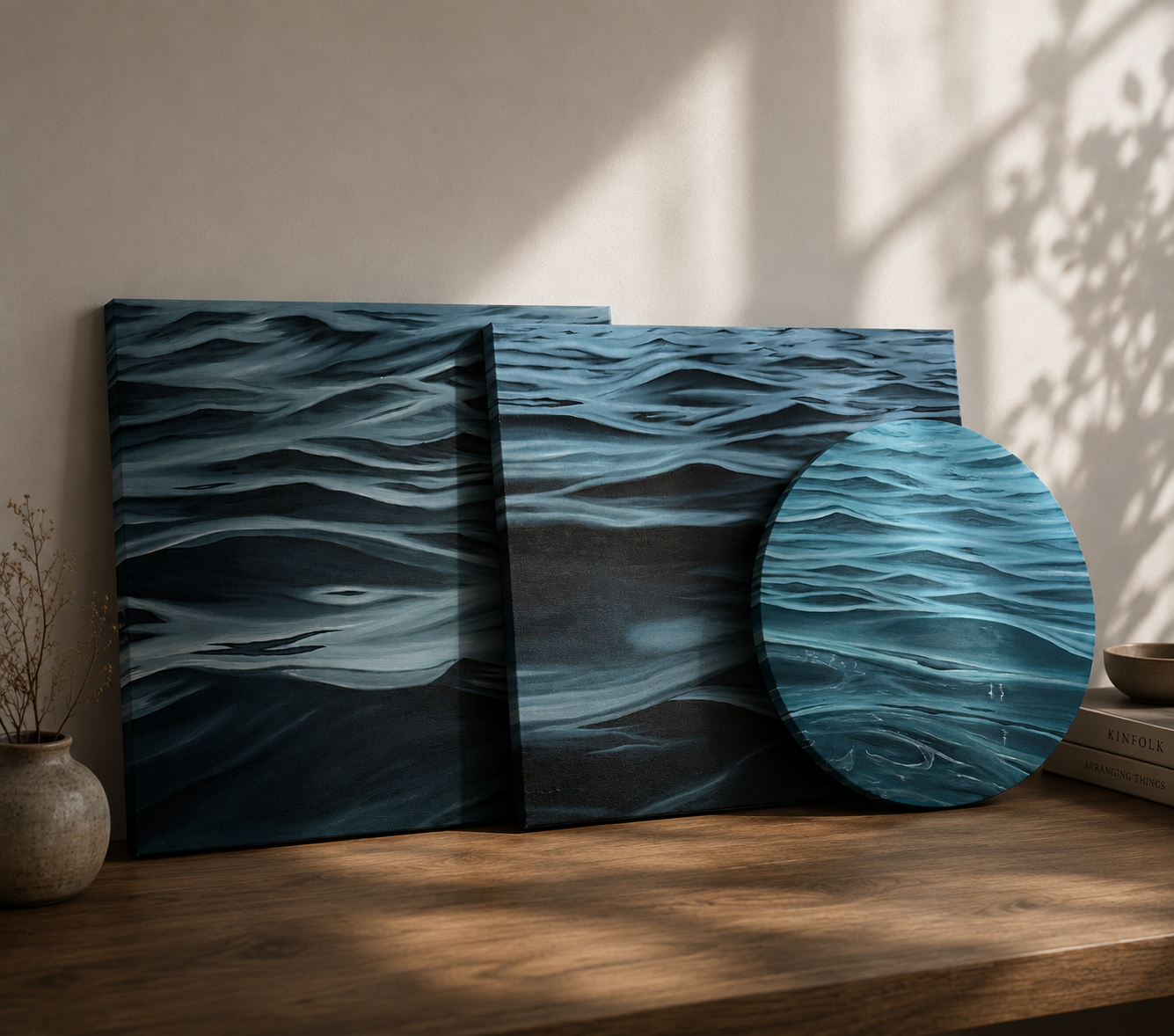 Drei Kunstwerke mit Meereswellenmuster, zwei rechteckige und ein runder, sind auf einem Holzregal platziert.