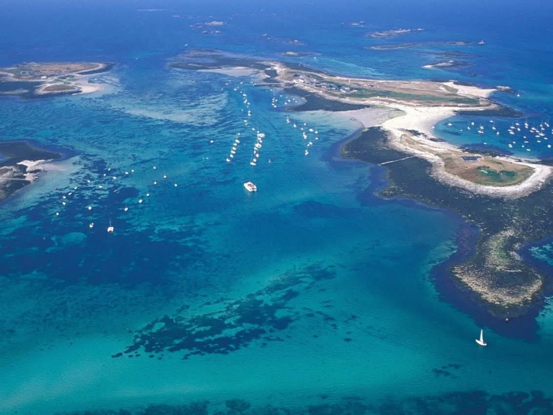 Aerial view of a coastal island with clear blue water and boats anchored around it.