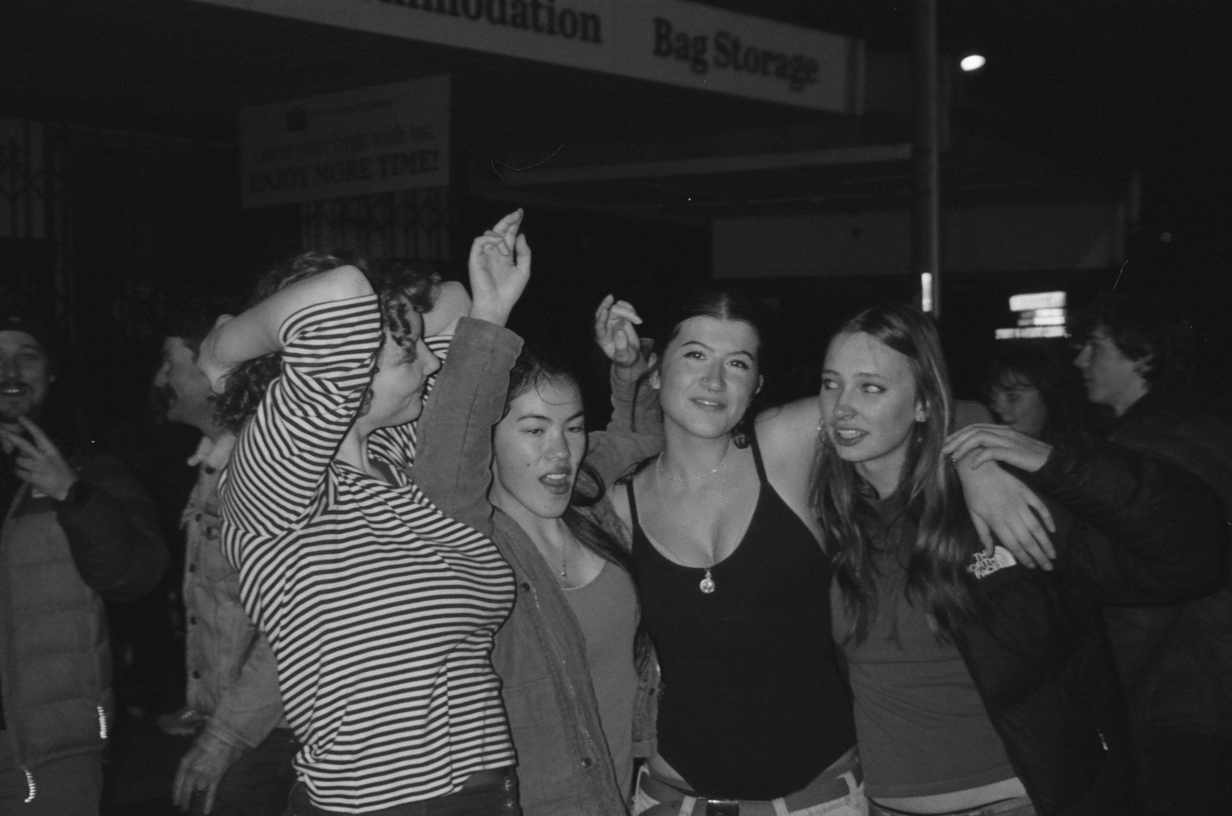 Group of young people at a party or nightclub, smiling and embracing each other.