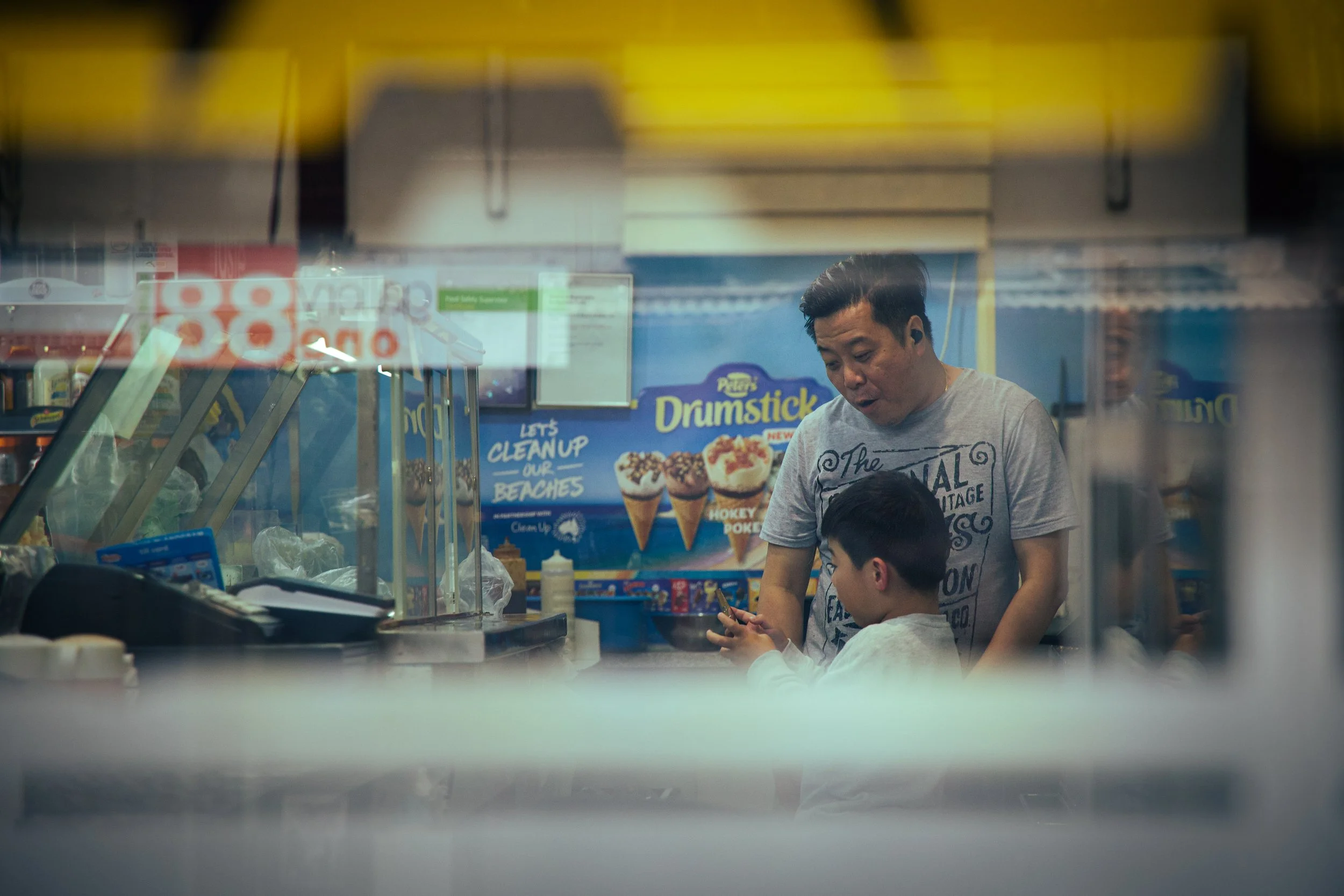 A man and a boy inside a fast food restaurant, seen through a glass window, with ice cream advertisements in the background.