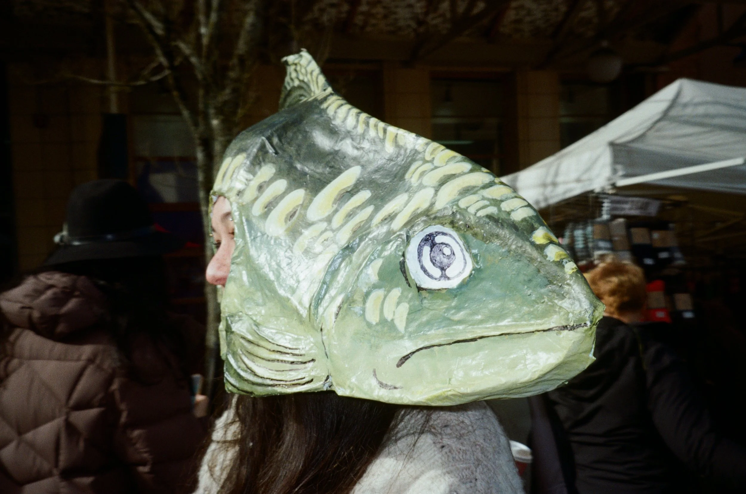 Person wearing a fish-shaped costume with detailed scales and eye design at a crowded indoor event.