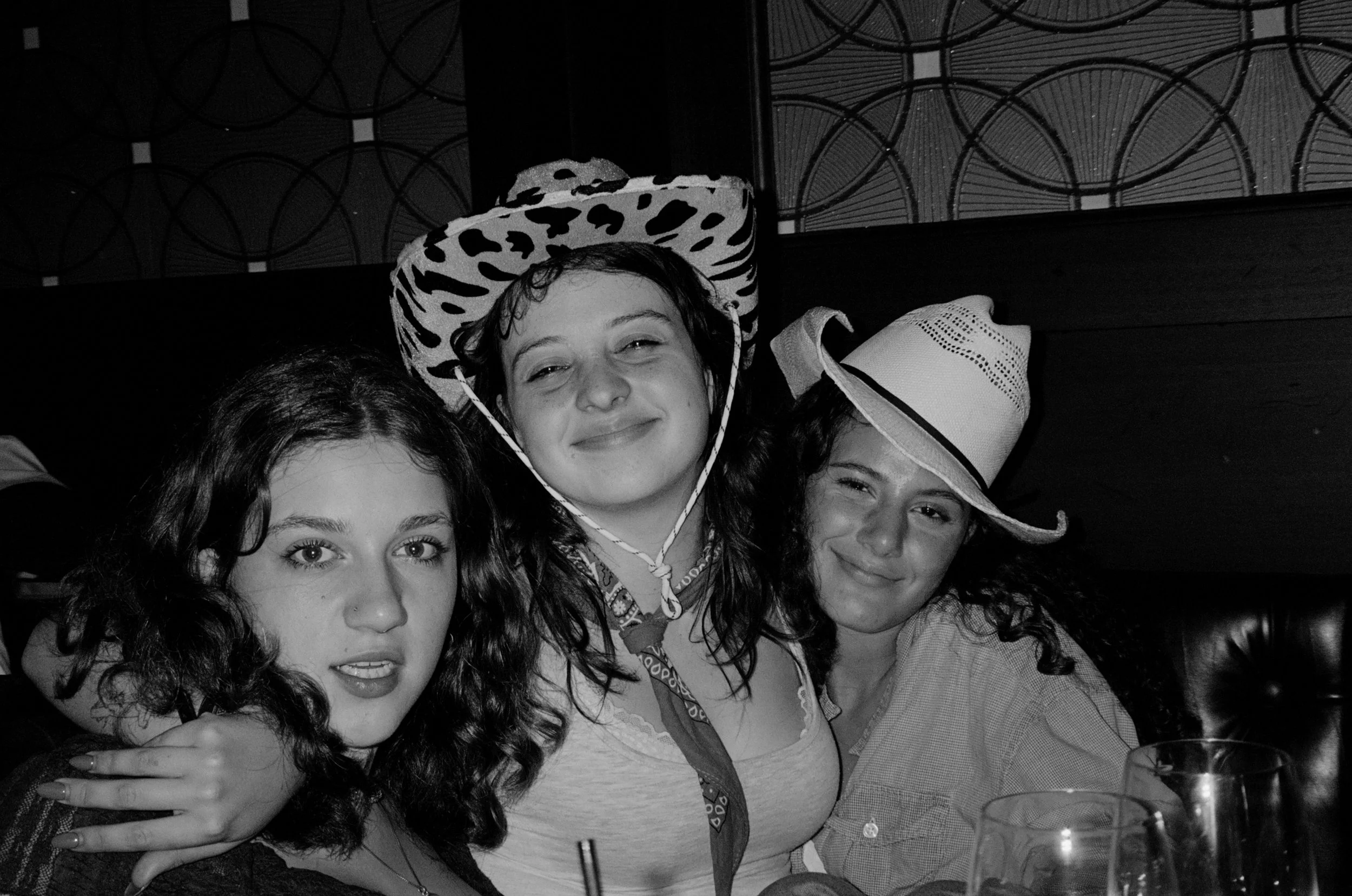 A group of young women posing for a black and white photo, some wearing hats, at a social gathering or party.