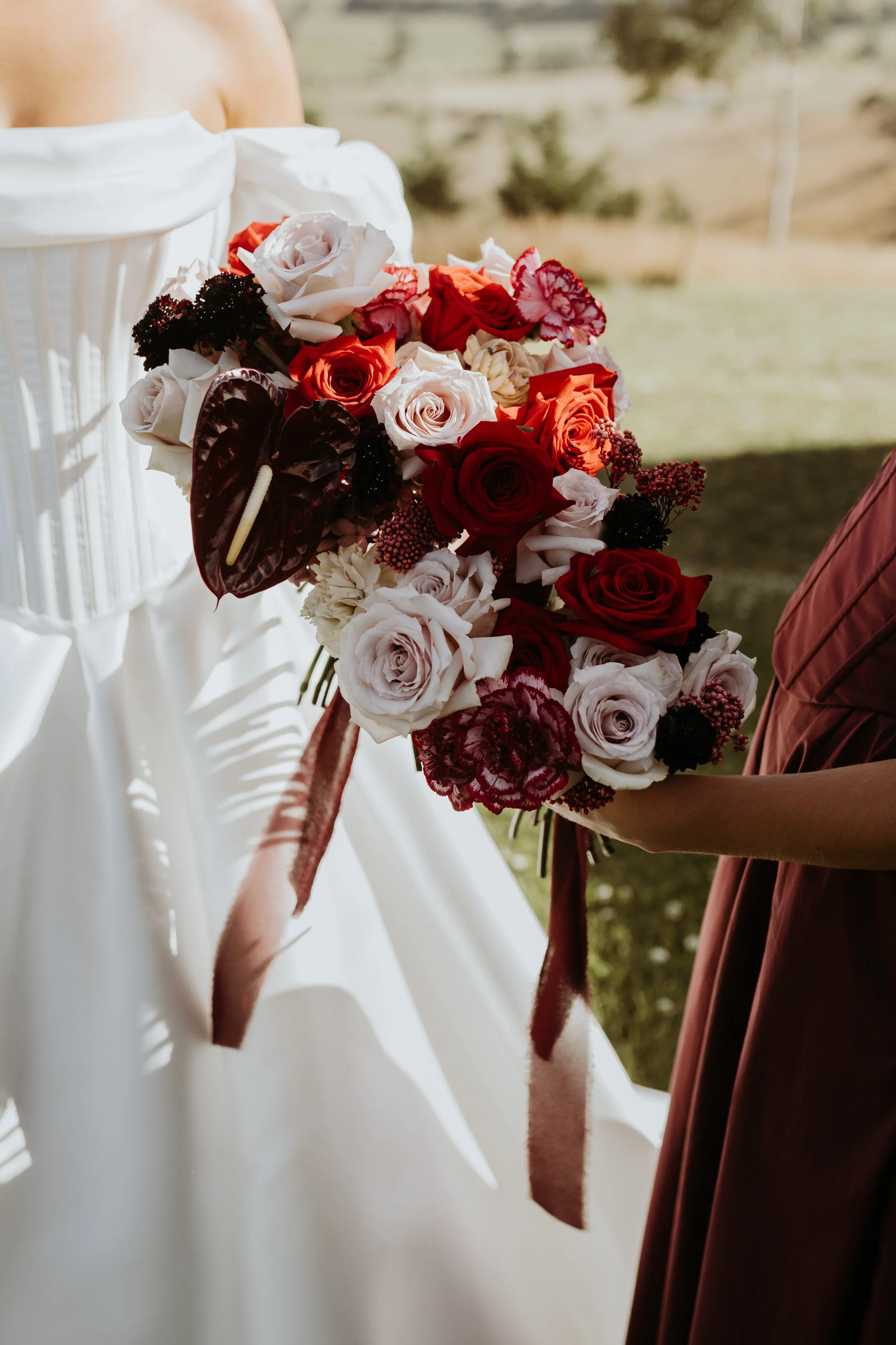 Close-up of a person holding a bouquet of mixed roses, including white, red, and pink, with some dark foliage, against a blurred outdoor background.