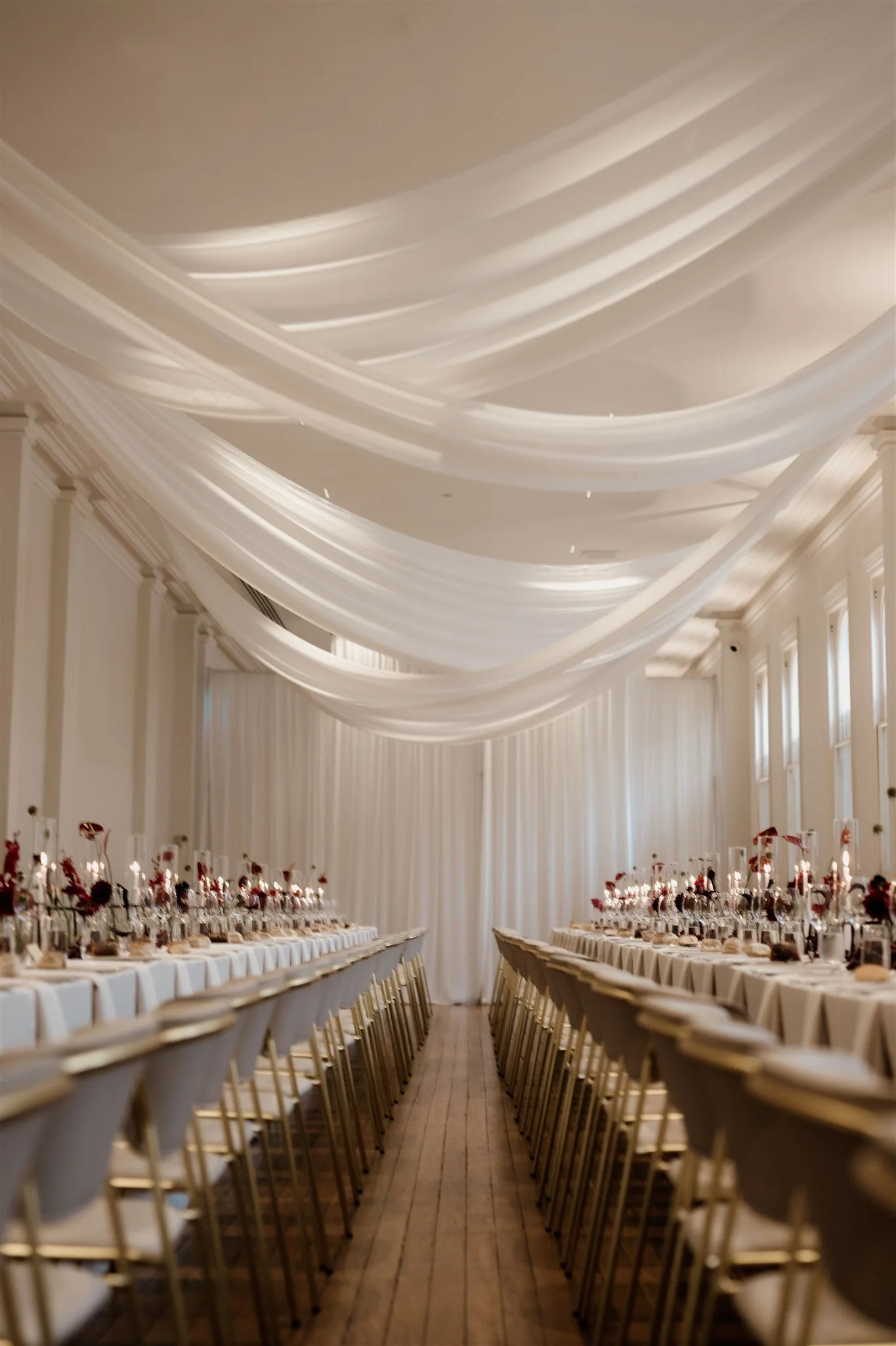 Elegant banquet hall decorated with white drapery on the ceiling, long dining tables set for a formal event, with chairs neatly arranged, and tall floral centerpieces at Sophias.