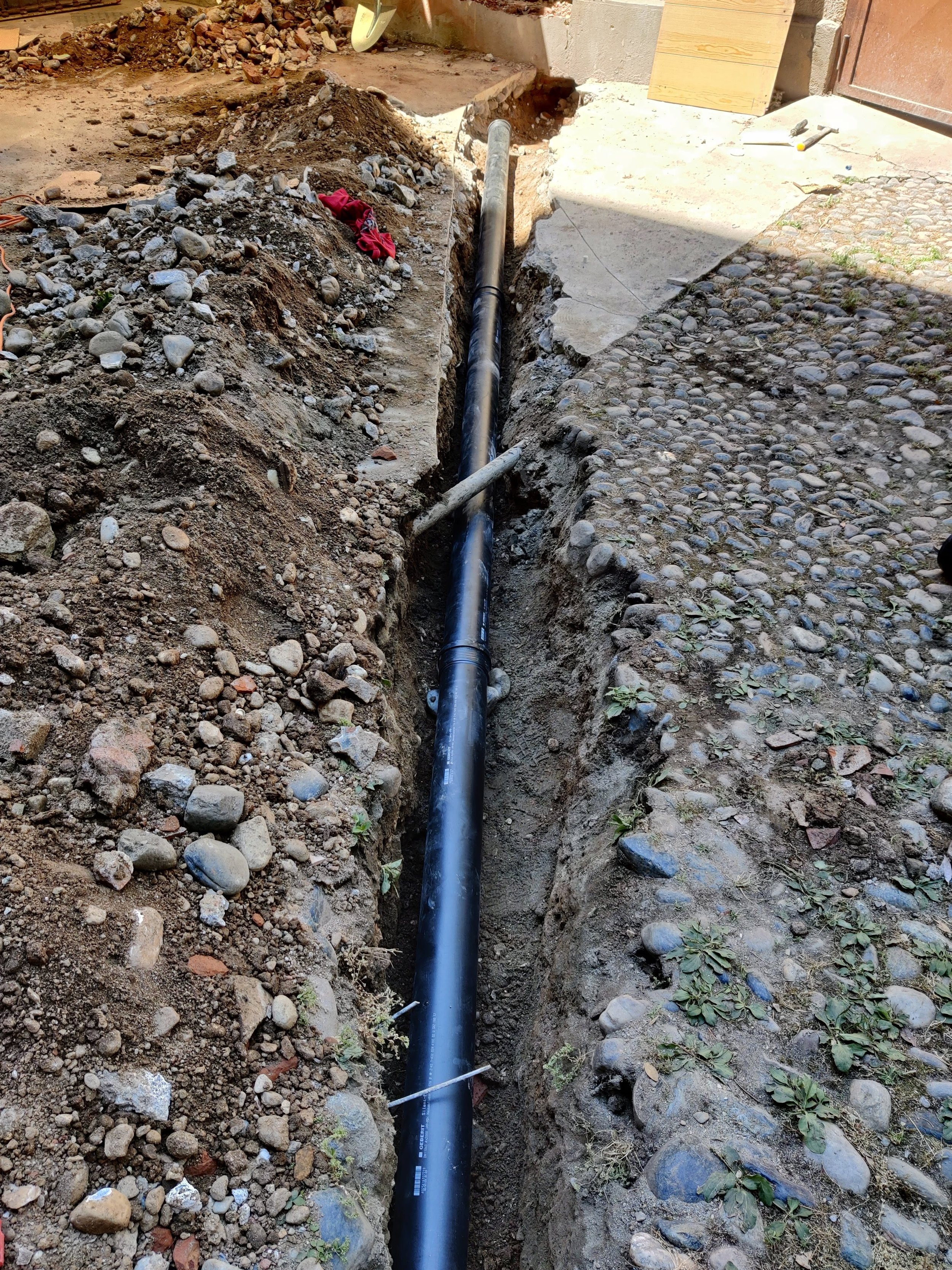 Una tubatura nera sotterranea installata in un cantiere, con scavi di terra e ciottoli ai lati.
