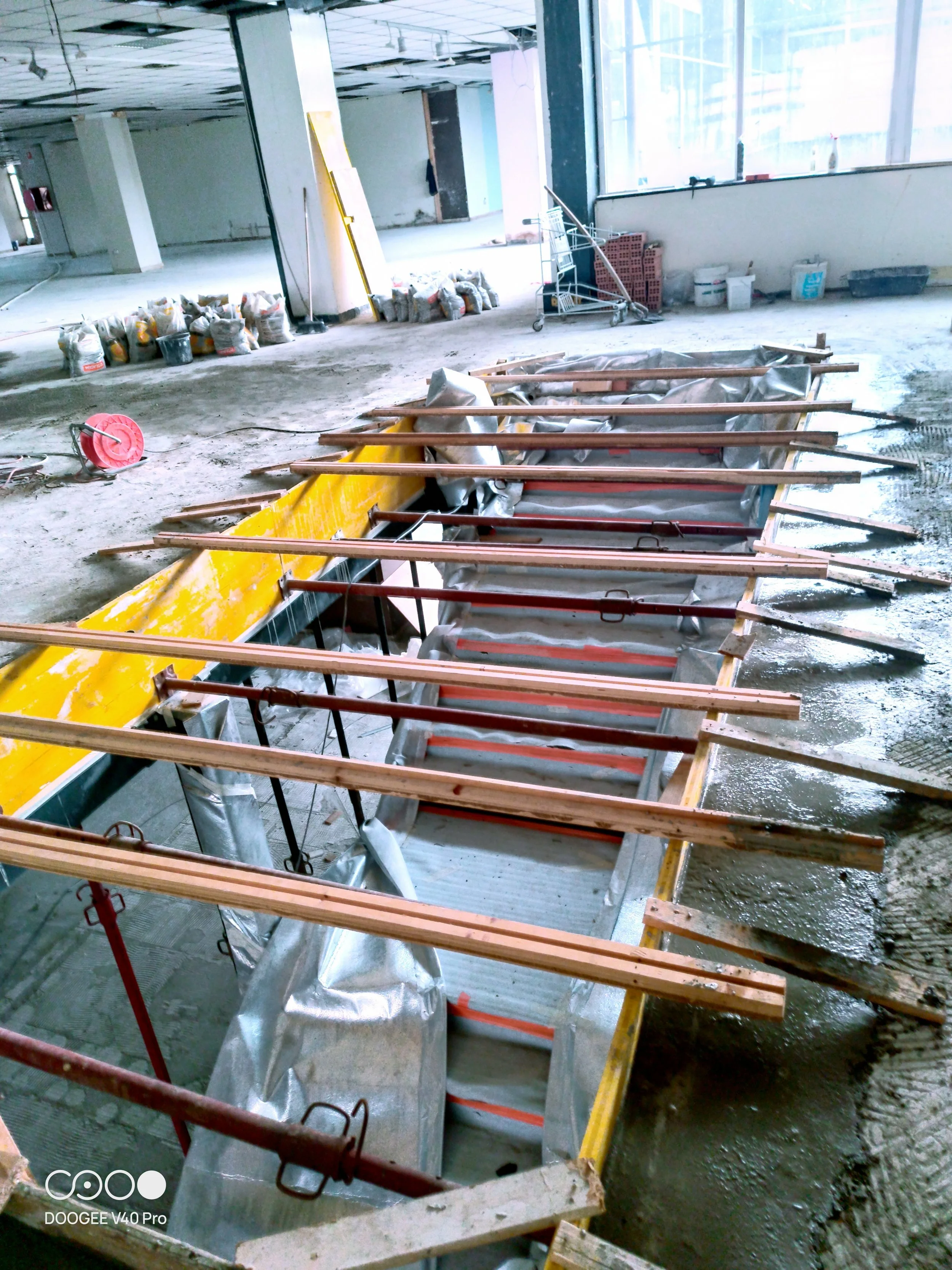 Interno di un cantiere con blocchi di cemento, attrezzi, tubi, e faretti sospesi, in fase di ristrutturazione.