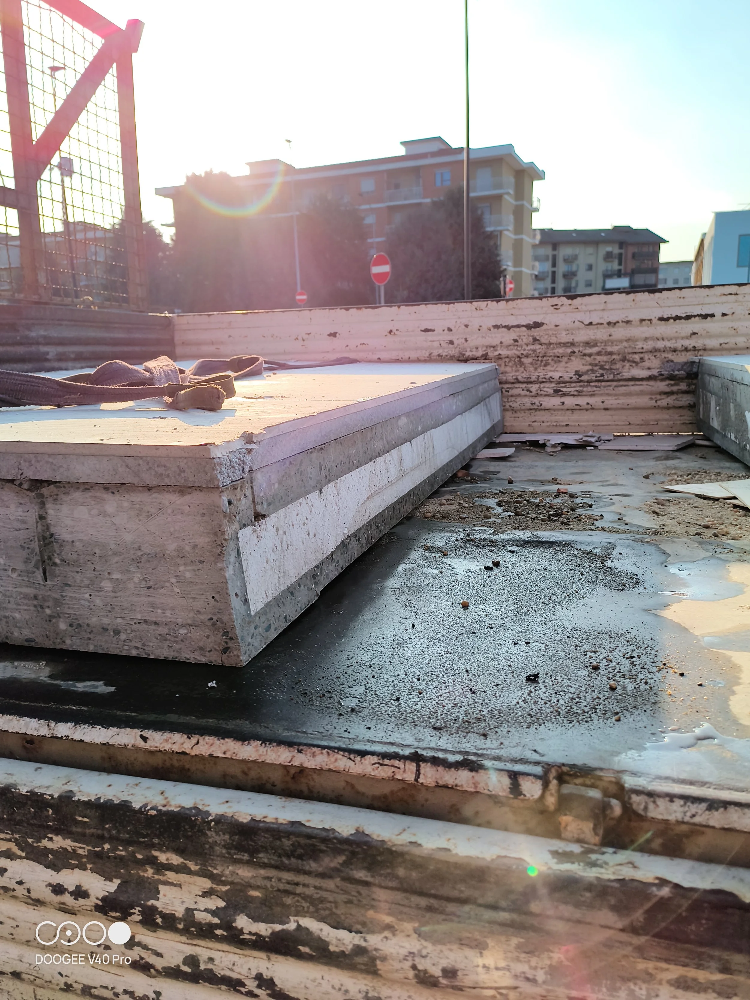 Immagine di un cantiere in cui ci sono blocchi di cemento e materiali per la costruzione, con edifici residenziali sullo sfondo, sotto la luce del sole.