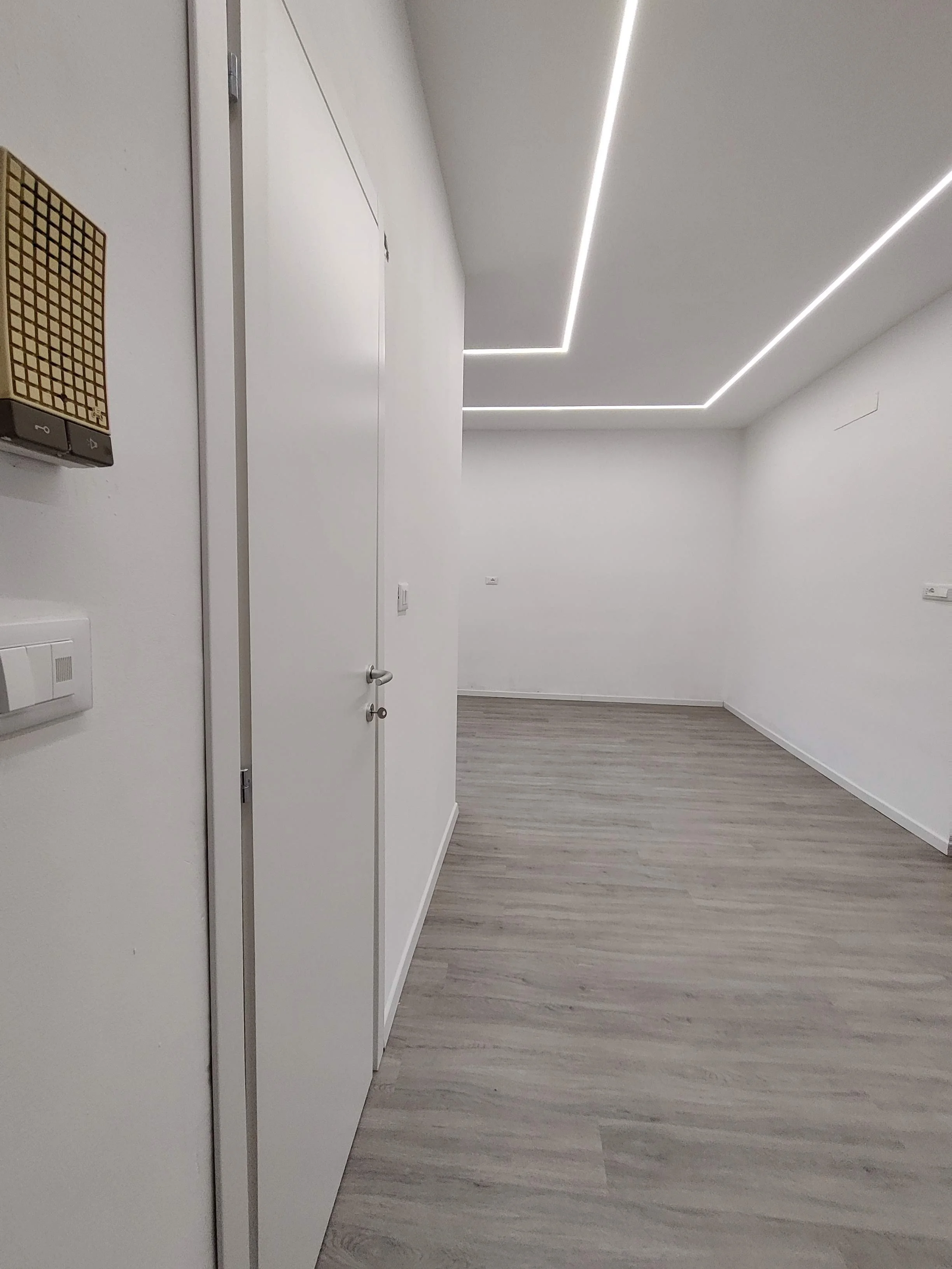 Stanza vuota con pareti bianche, pavimento in legno chiaro, illuminazione LED sul soffitto in uno stile moderno.