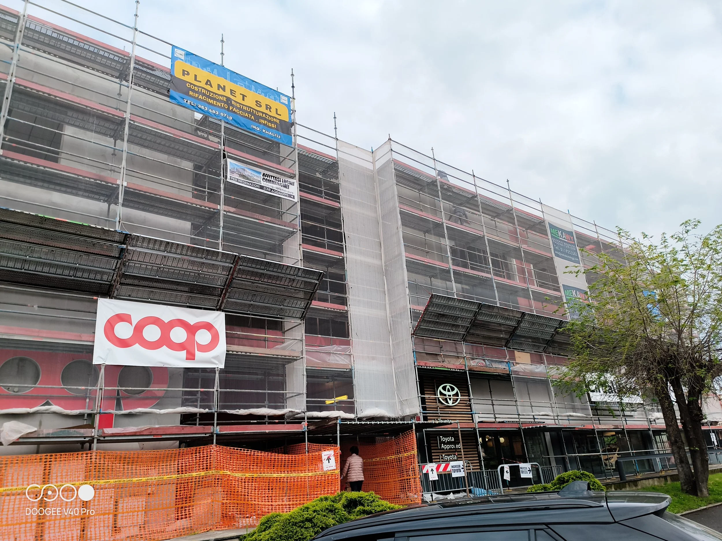 Edificio in costruzione con impalcature e vari cartelli pubblicitari, tra cui uno di COOP e uno di Toyota.