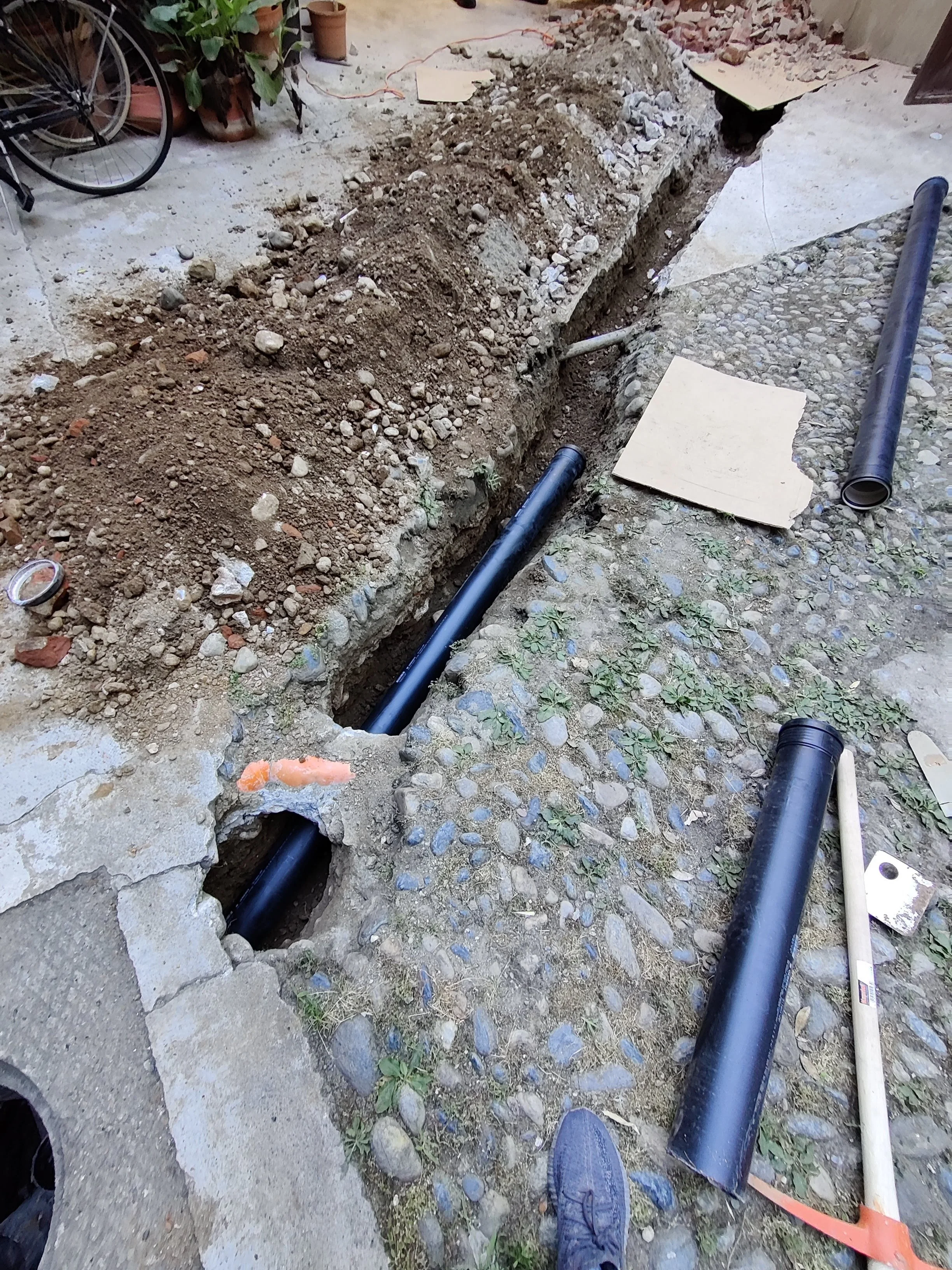 Scavo in corso con tubi neri e attrezzi su terreno di pietre e terra, utilizzati per lavori di costruzione o riparazione