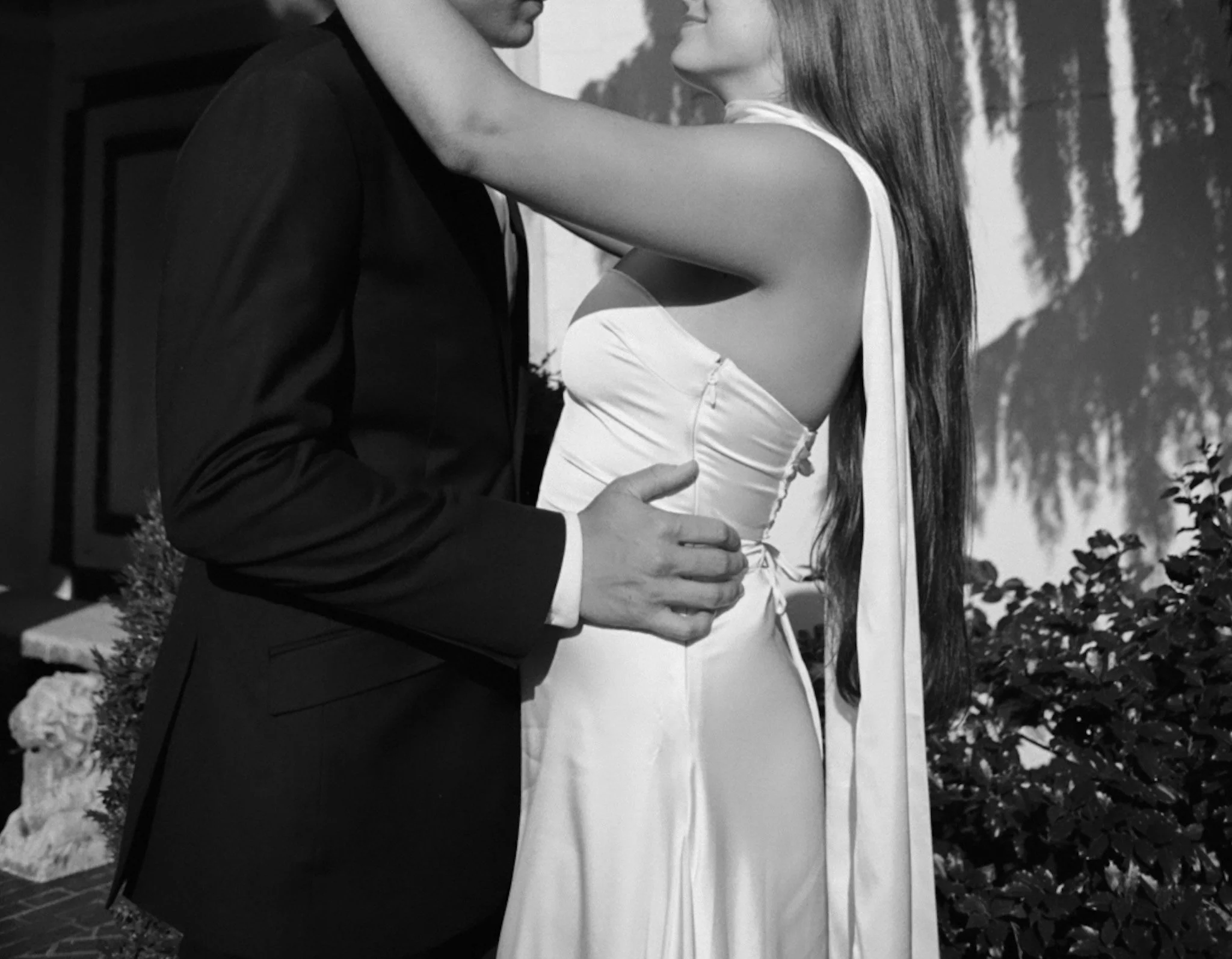 A black and white photo of a couple in formal attire embracing each other outdoors.