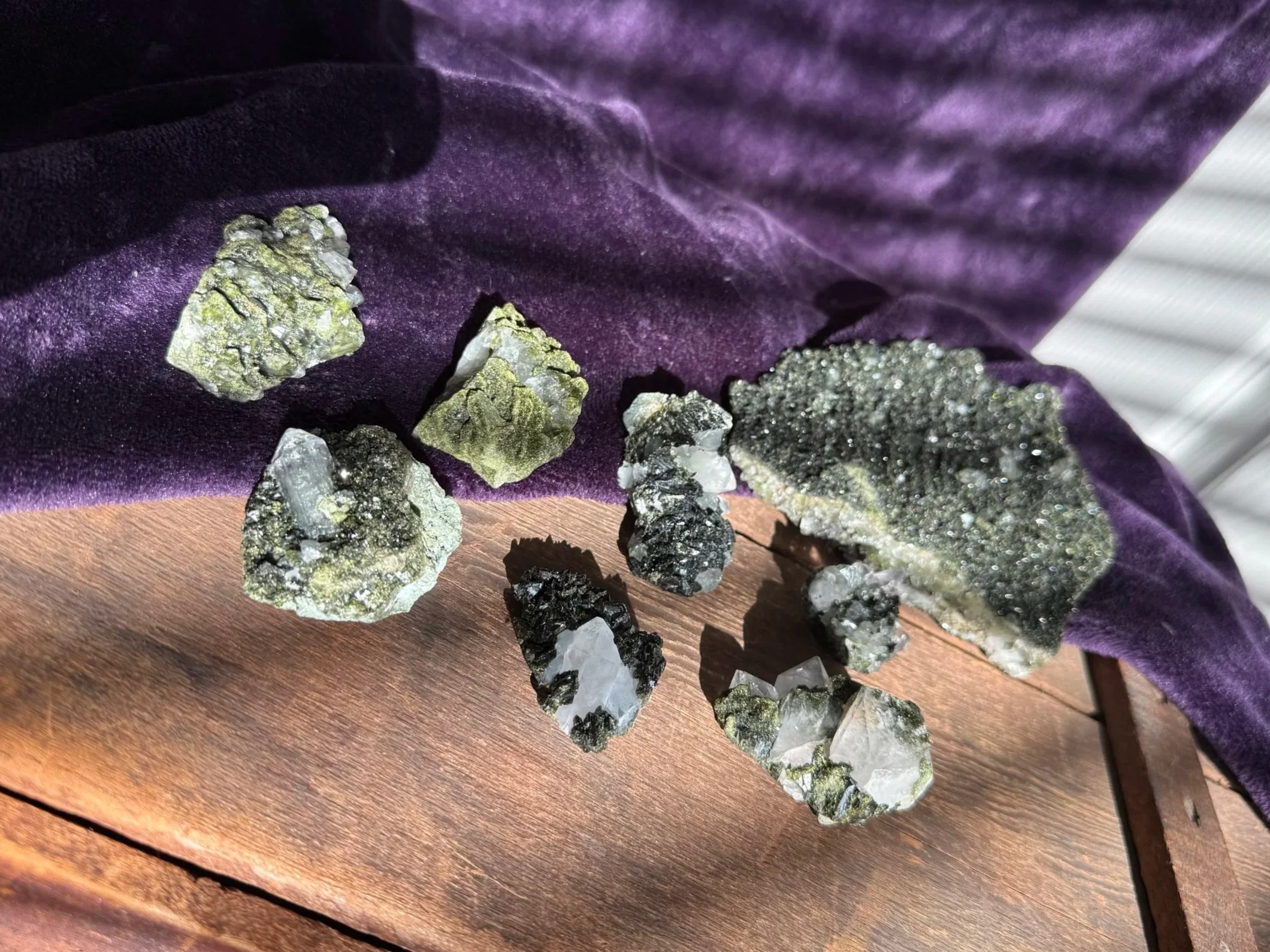 Various mineral and crystal specimens resting on a purple cloth and wooden surface.