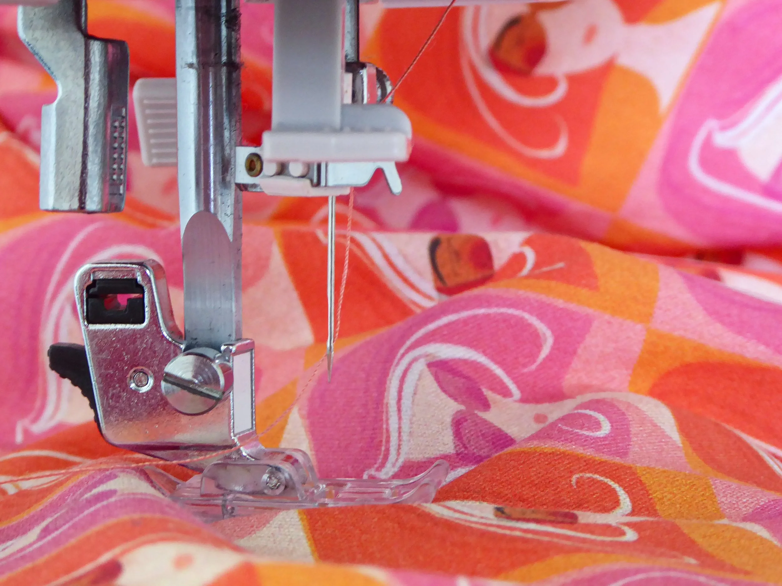 Close-up of a sewing machine needle and presser foot on colorful orange and pink fabric with retro image of a woman with red hair pattern