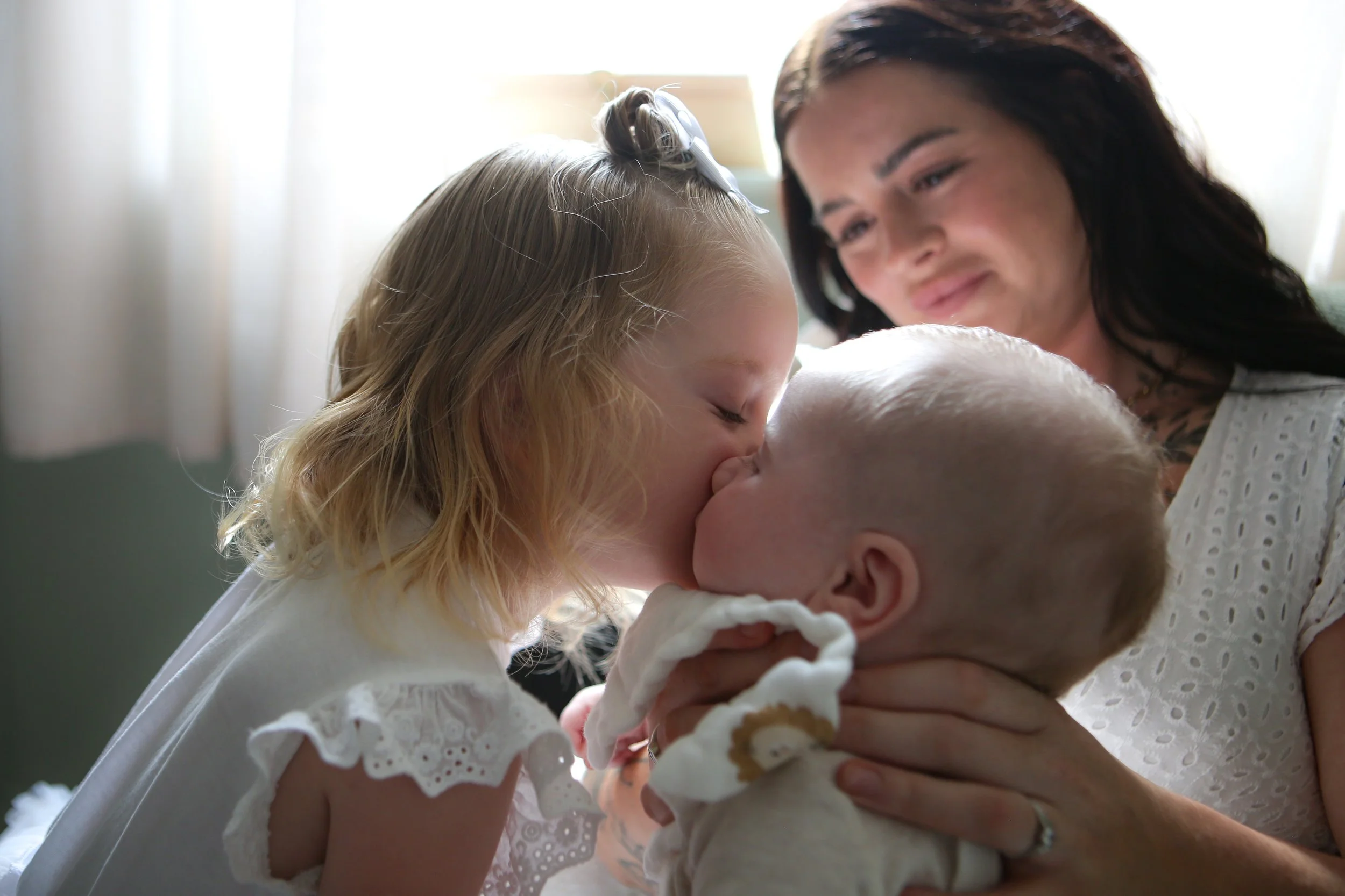 Een jonge vrouw en haar twee jonge kinderen omhelzen en kussen elkaar liefkozend binnen in de woning.