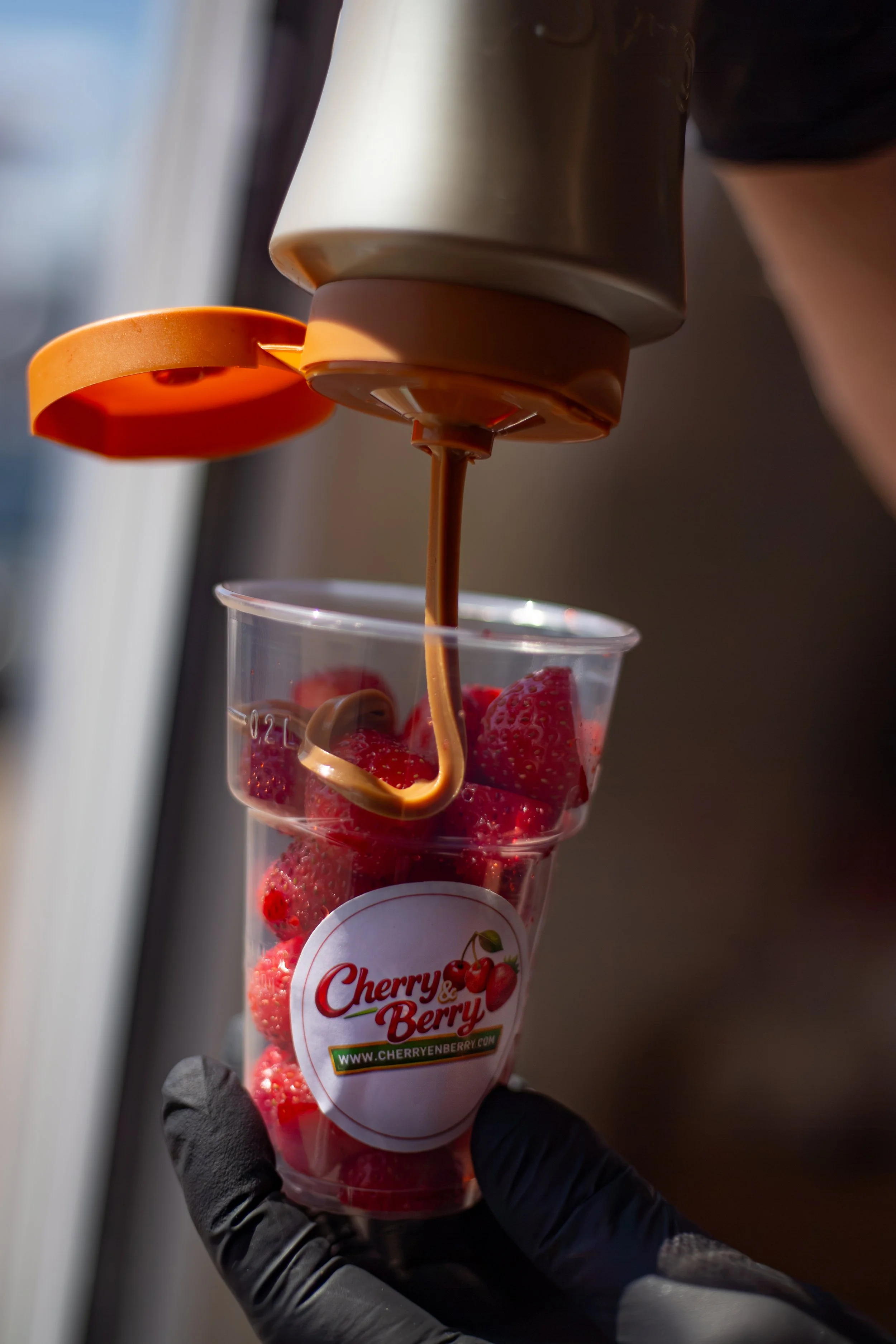 Een plastic beker met aardbeien en chocoladesaus, met chocoladesaus die wordt uitgegoten.
