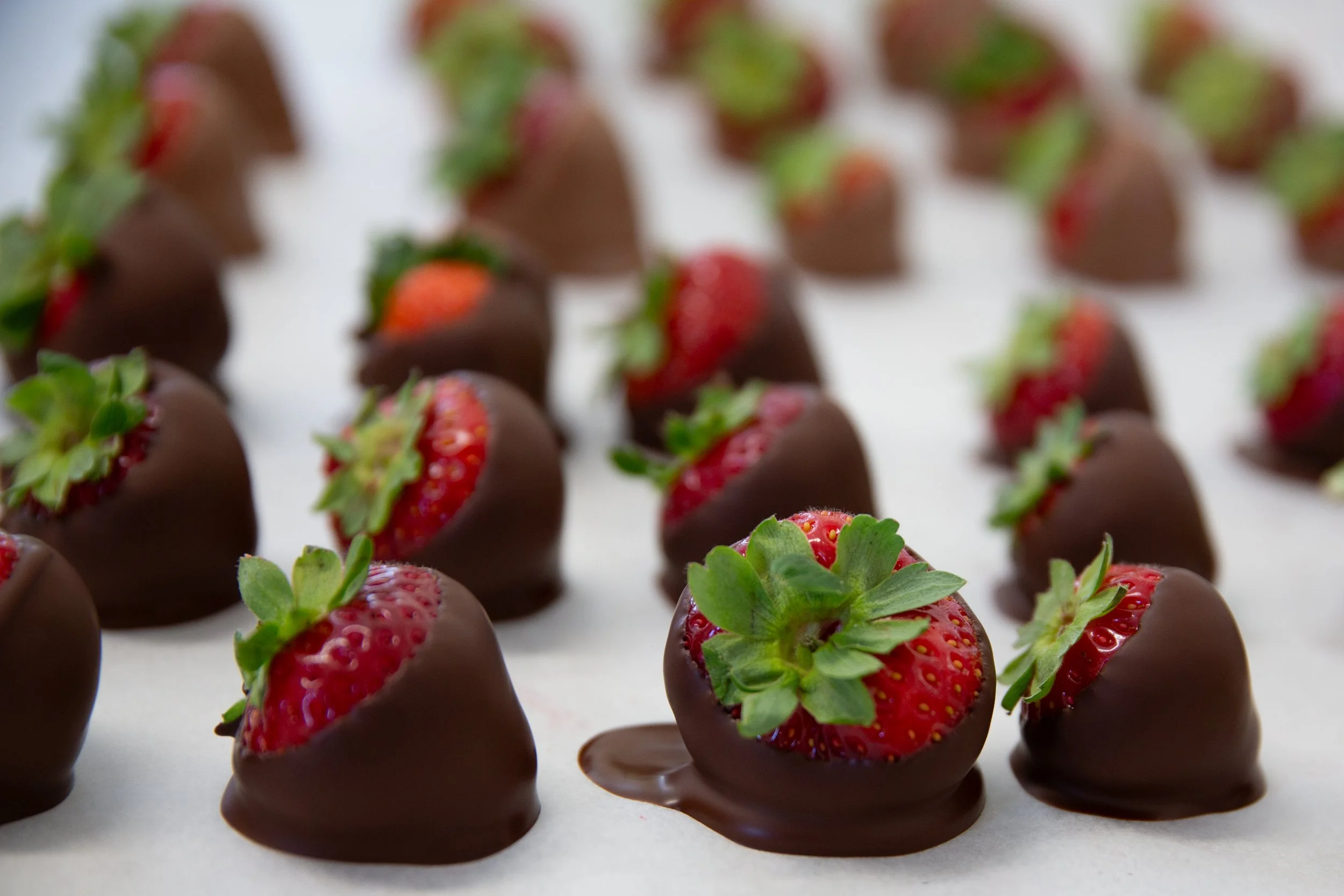 Chocoladekuipjes met aardbeien erin, bedekt met chocolade, uitgestald op een witte achtergrond.
