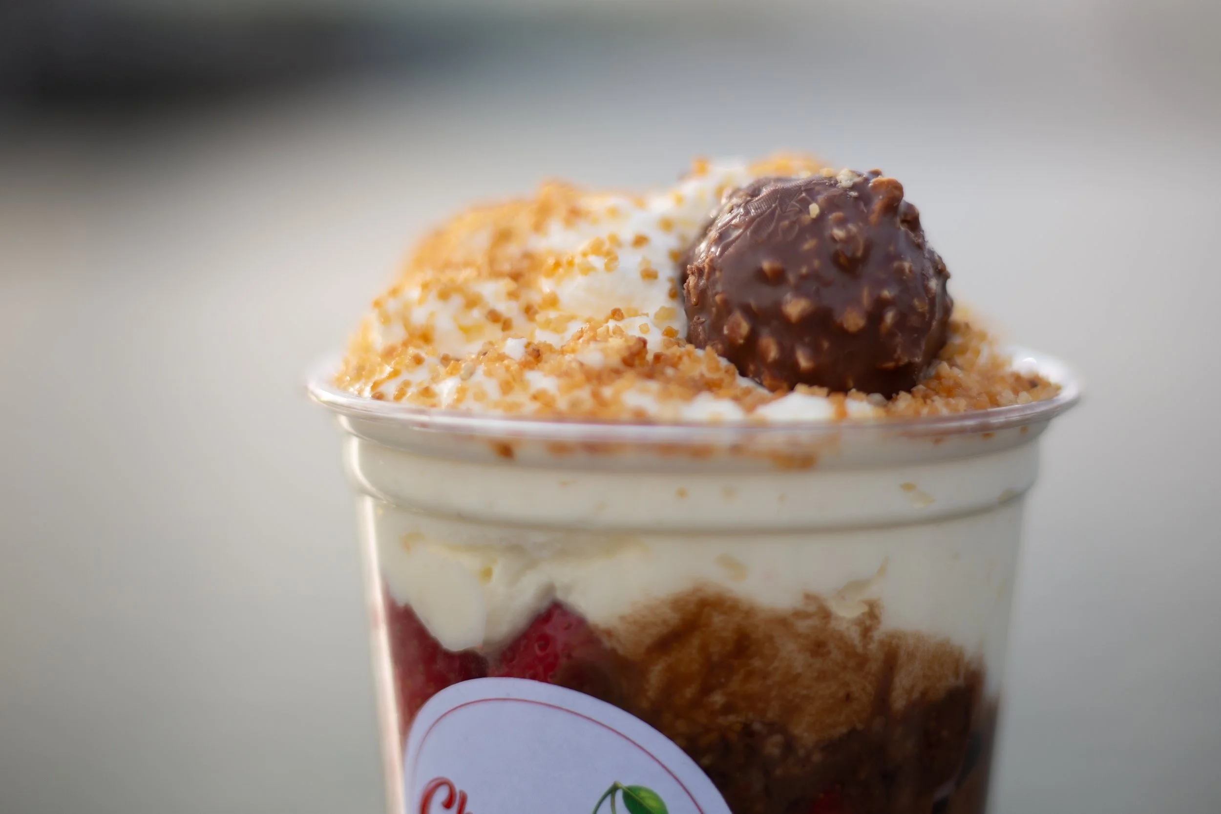 Een glas met tiramisu met slagroom, gehakte noten en een chocoladebal bovenop.