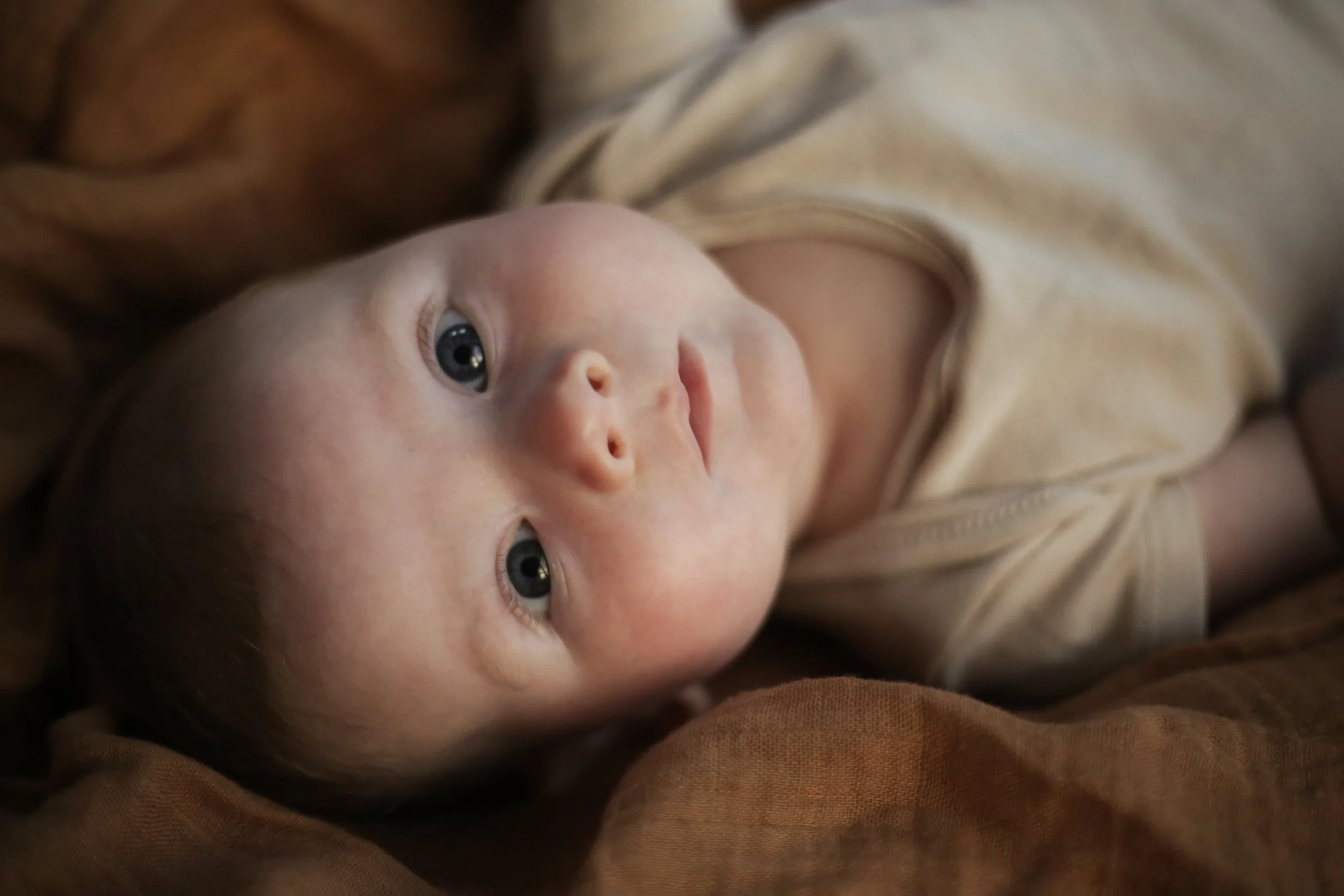 Close-up van een baby met blauwe ogen, liggend op een zachte ondergrond.