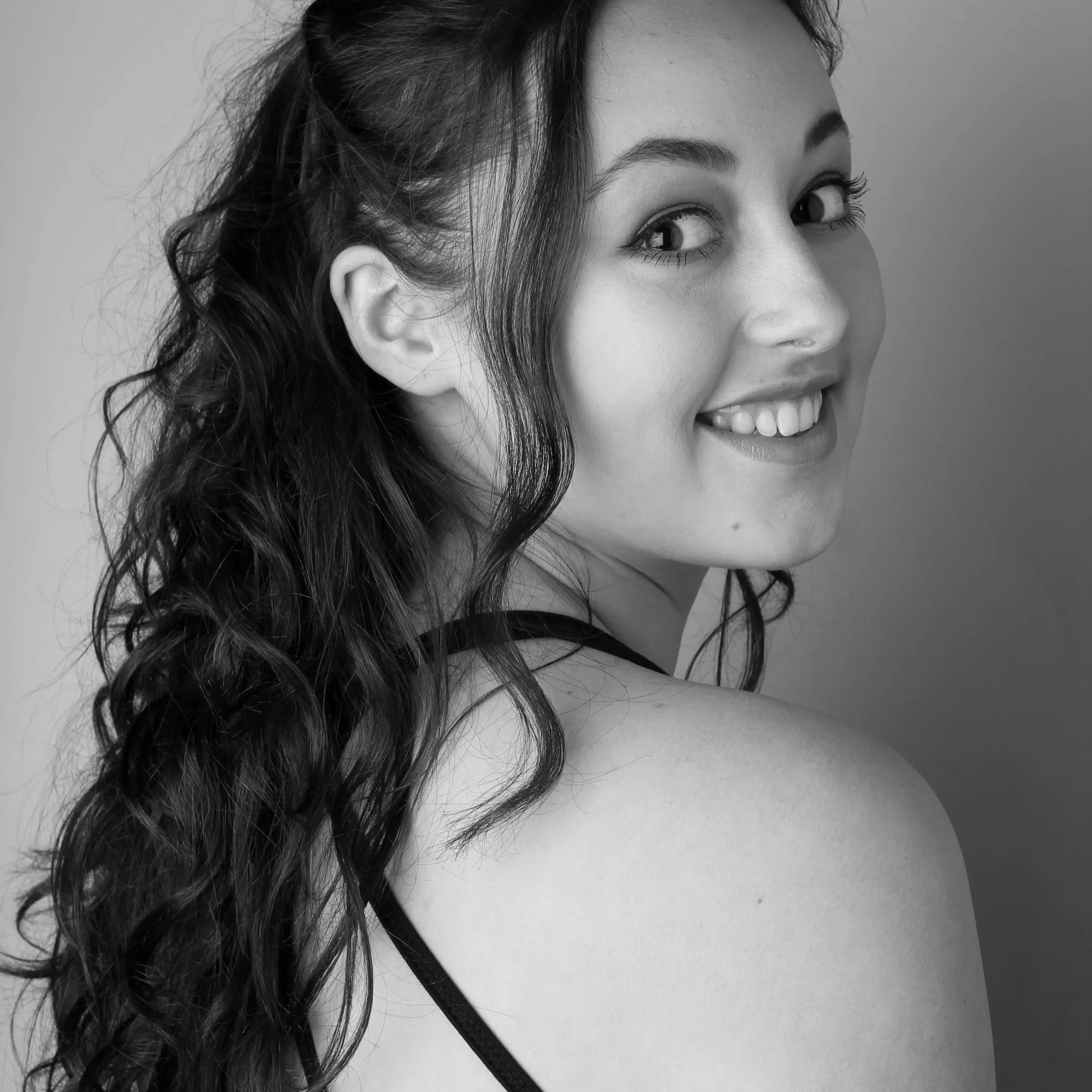 Zwarte en witte portretfoto van een lachende vrouw met lang, golvend haar, kijkend naar links.