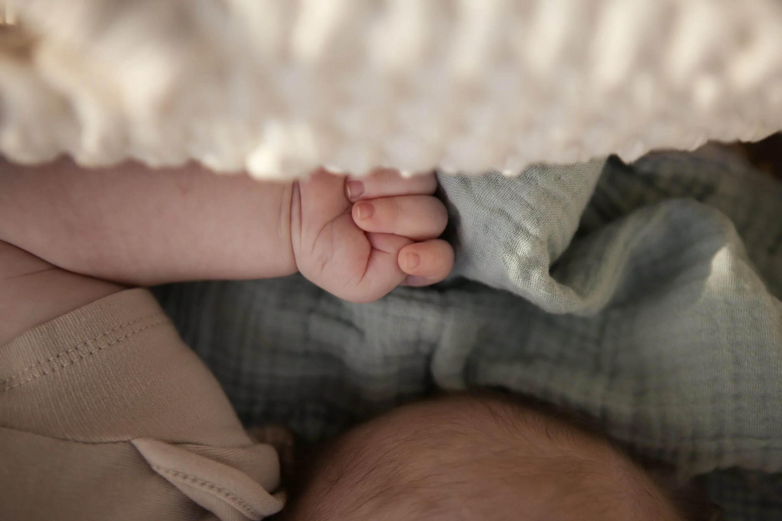Close-up van een hand die een baby vastpakt, met een vlekkerig ondergrond eronder.