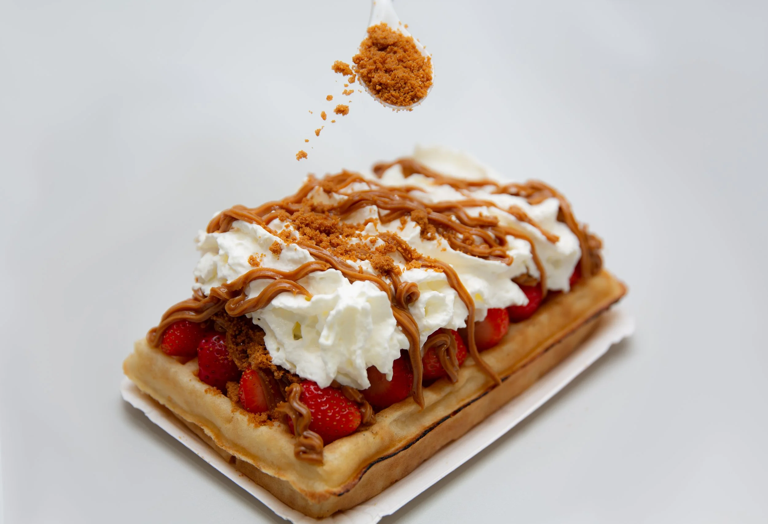 Aardbeientaartje met slagroom, chocolade en krokante topping, met stukjes aardbei zichtbaar onder de slagroom.