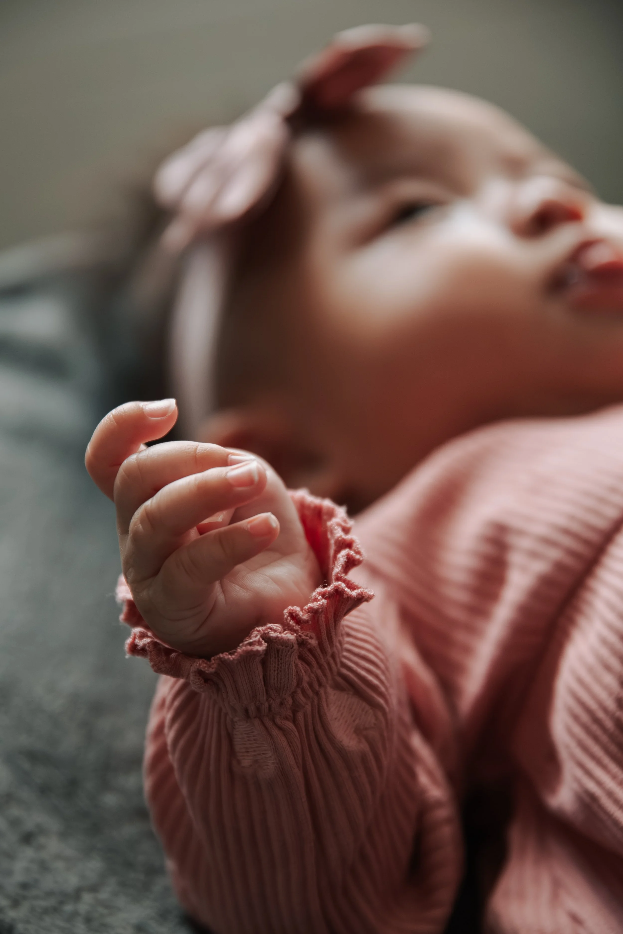 Close-up van een lachende baby met een hand dicht bij het gezicht, gekleed in een roze kledingstuk met ruches.