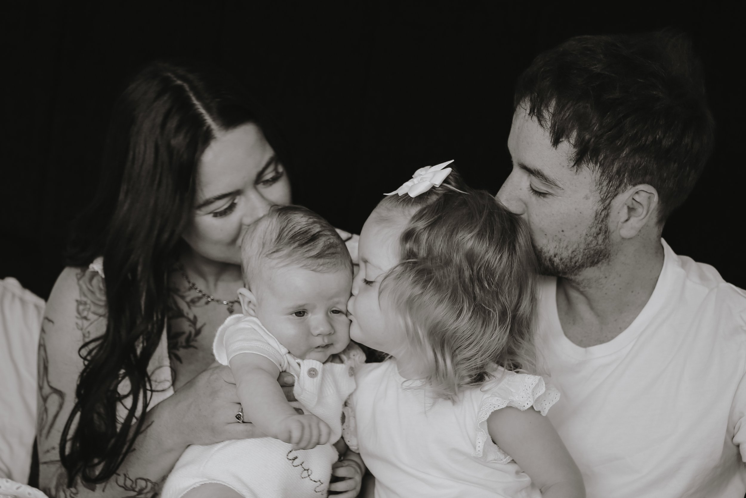 Een zwart-witte foto van een familie die knuffelt en een kus deelt.