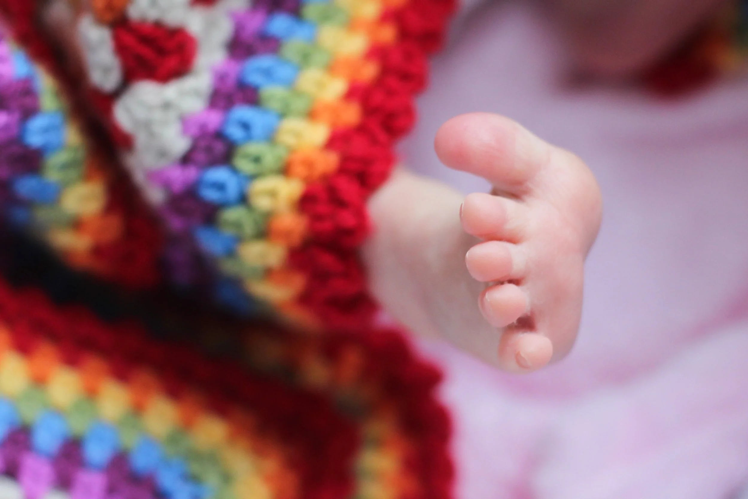 Close-up van een kinderhand die bijna een kleurrijk gehaakt motief aanraakt, met veel verschillende kleuren garen.
