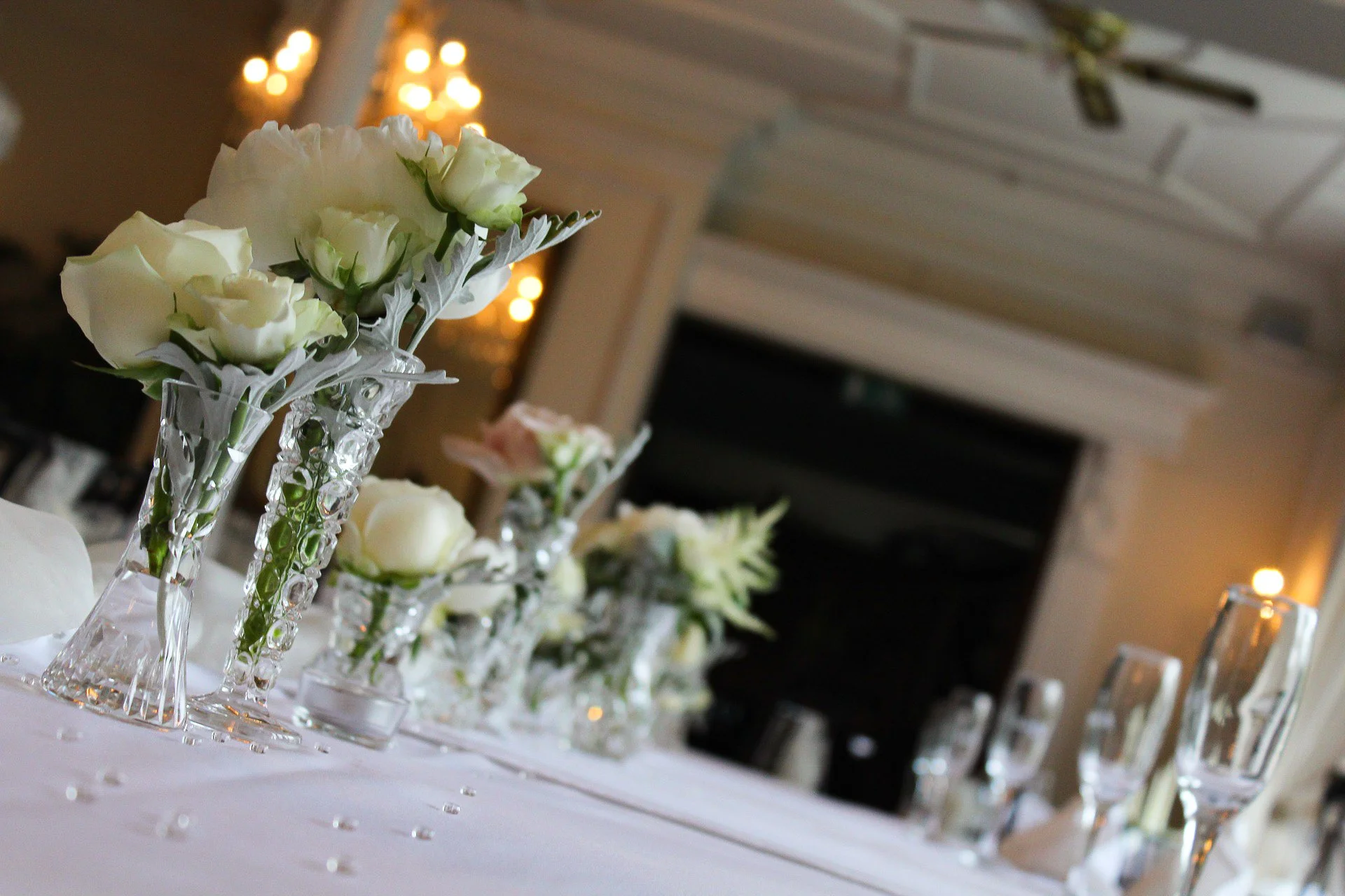 Witbloemige bloemen in kristallen vazen op een wit tafelkleed, versierd met kleine glinsterende decoraties, binnenshuis met warme verlichting op de achtergrond.