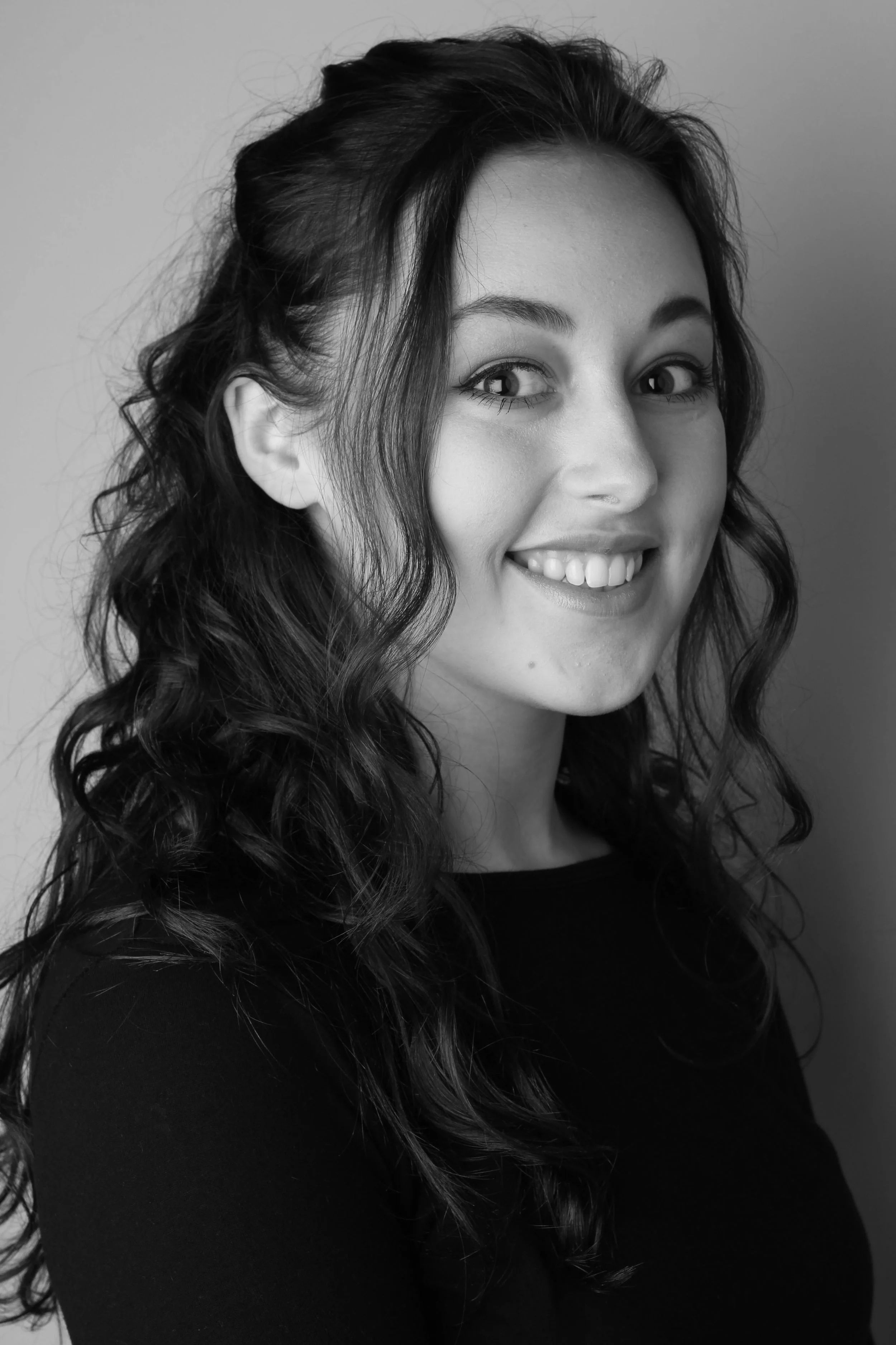 Portret van een jonge vrouw met lang, golvend haar, glimlachend, zwart-wit foto.