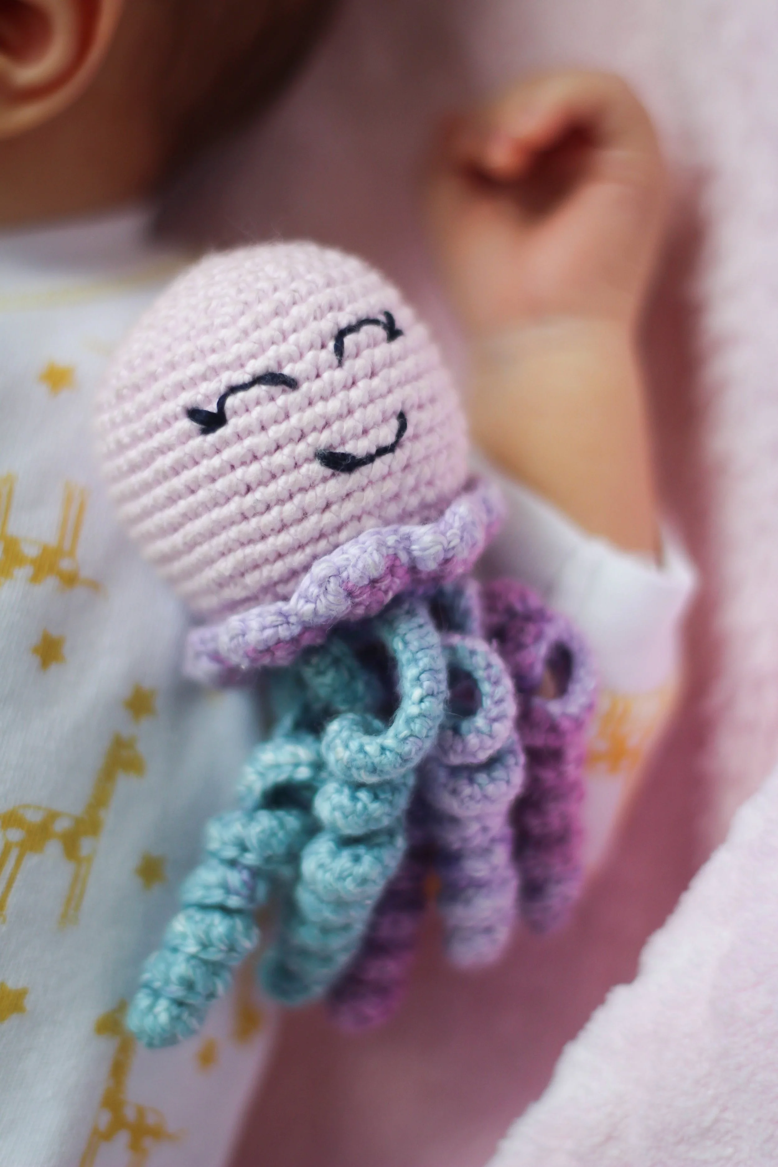 Close-up van een babyhoofd met een vinger die de wang beroert, en een knuffel met een lachend gezichtje in de buurt.