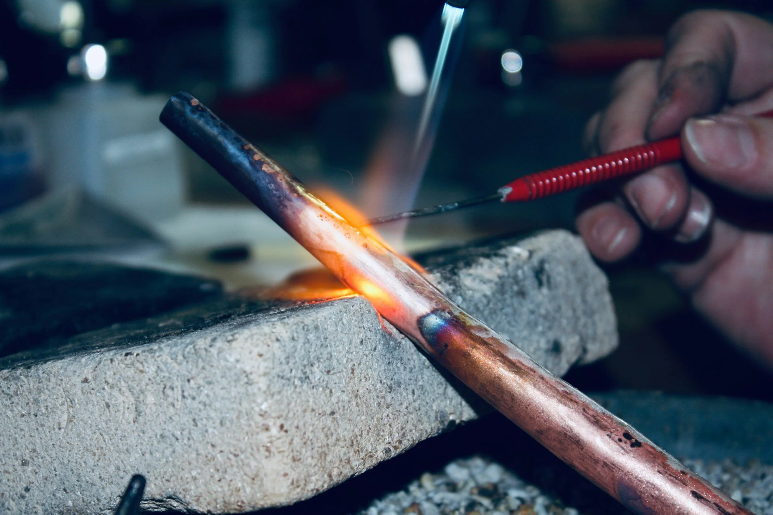 A person is welding a metal pipe to a plate, with bright sparks and a concentrated hand holding the welding tool.