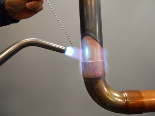 A person welding a metal pipe with a torch, creating sparks and blue light.